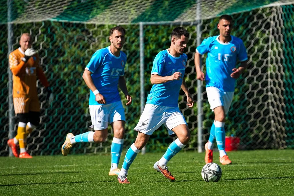 Fußballspieler in blauen Trikots beim Training auf dem Fußballfeld, mit einem Tor im Hintergrund.