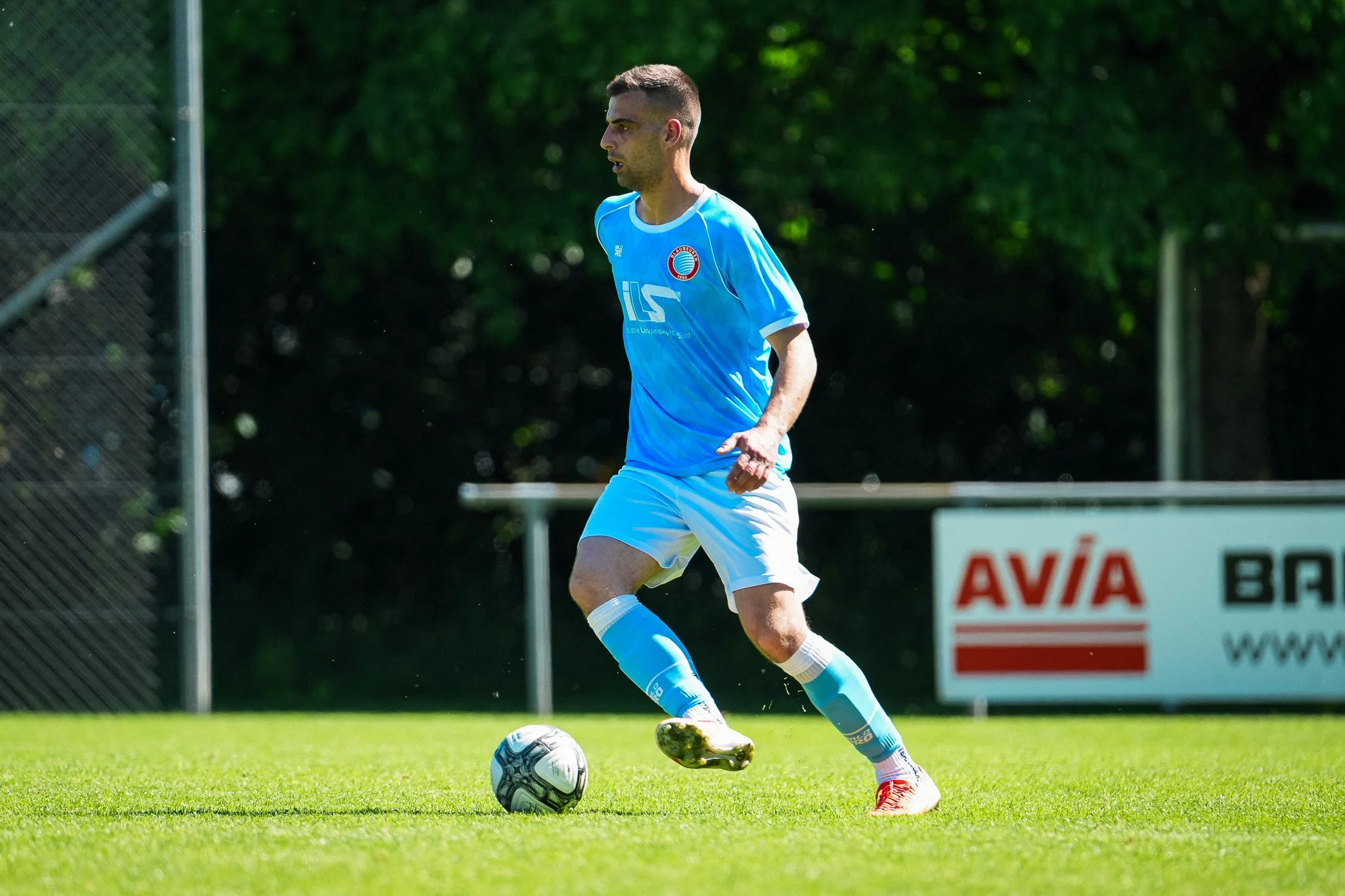 Fußballspieler in blauer Trikot auf dem Fußballplatz, der den Ball kontrolliert.