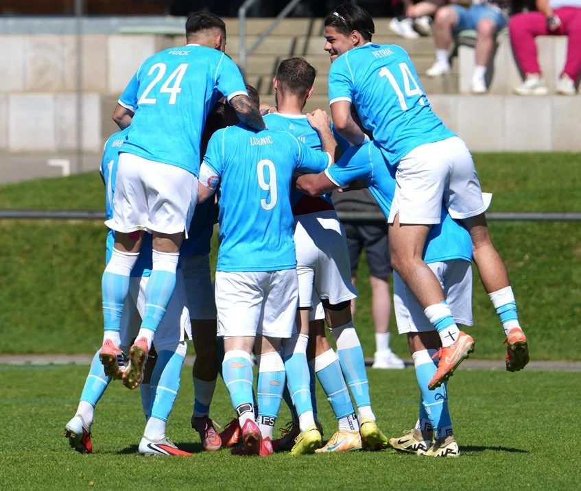 Fußballspieler feiern ein Tor auf dem Spielfeld, umgeben von Zuschauern im Stadion.