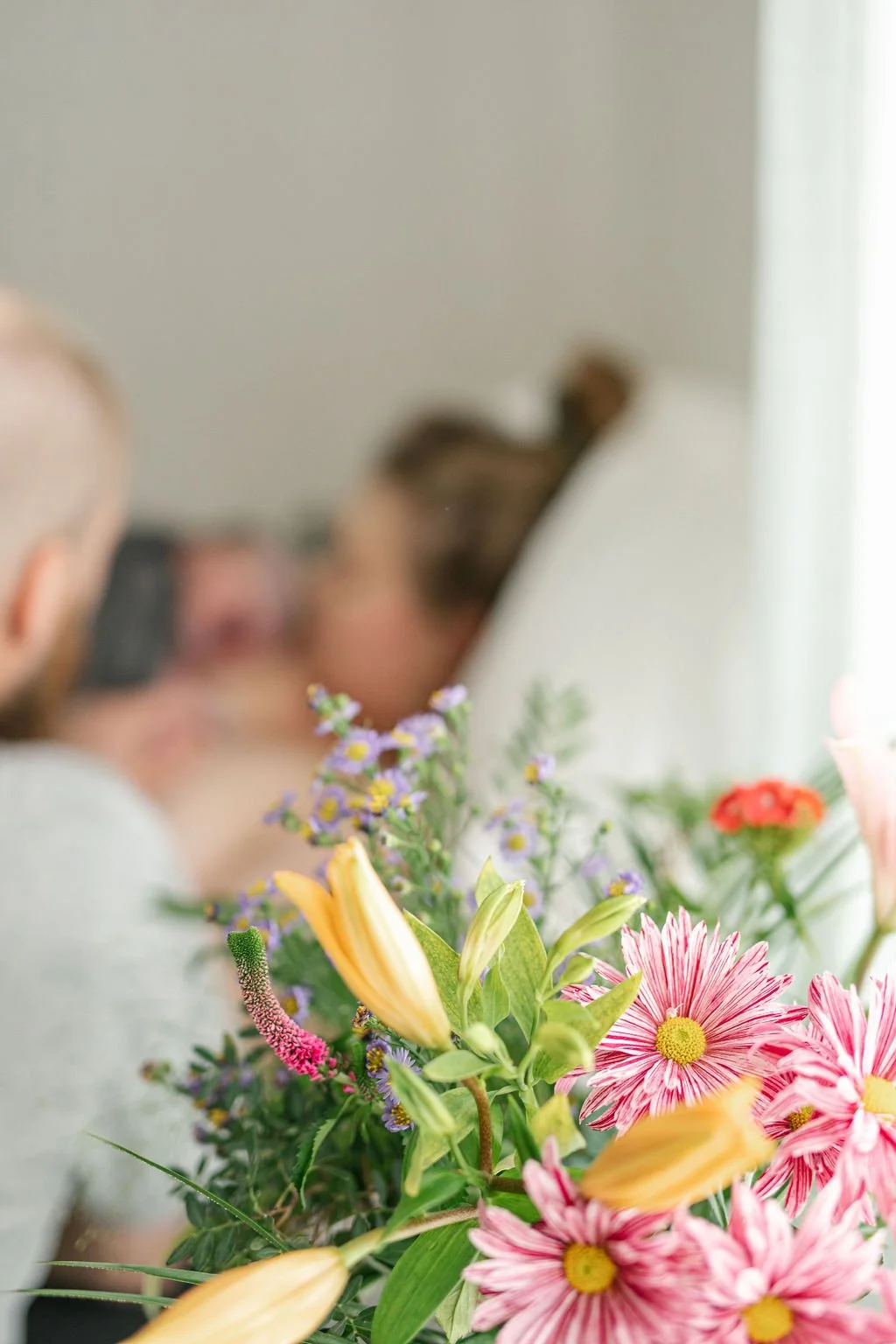 Vastasynnyttänyt ja vauva, synnytys ohi ja puoliso tukemassa vieressä. Edustalla kukkakimppu.