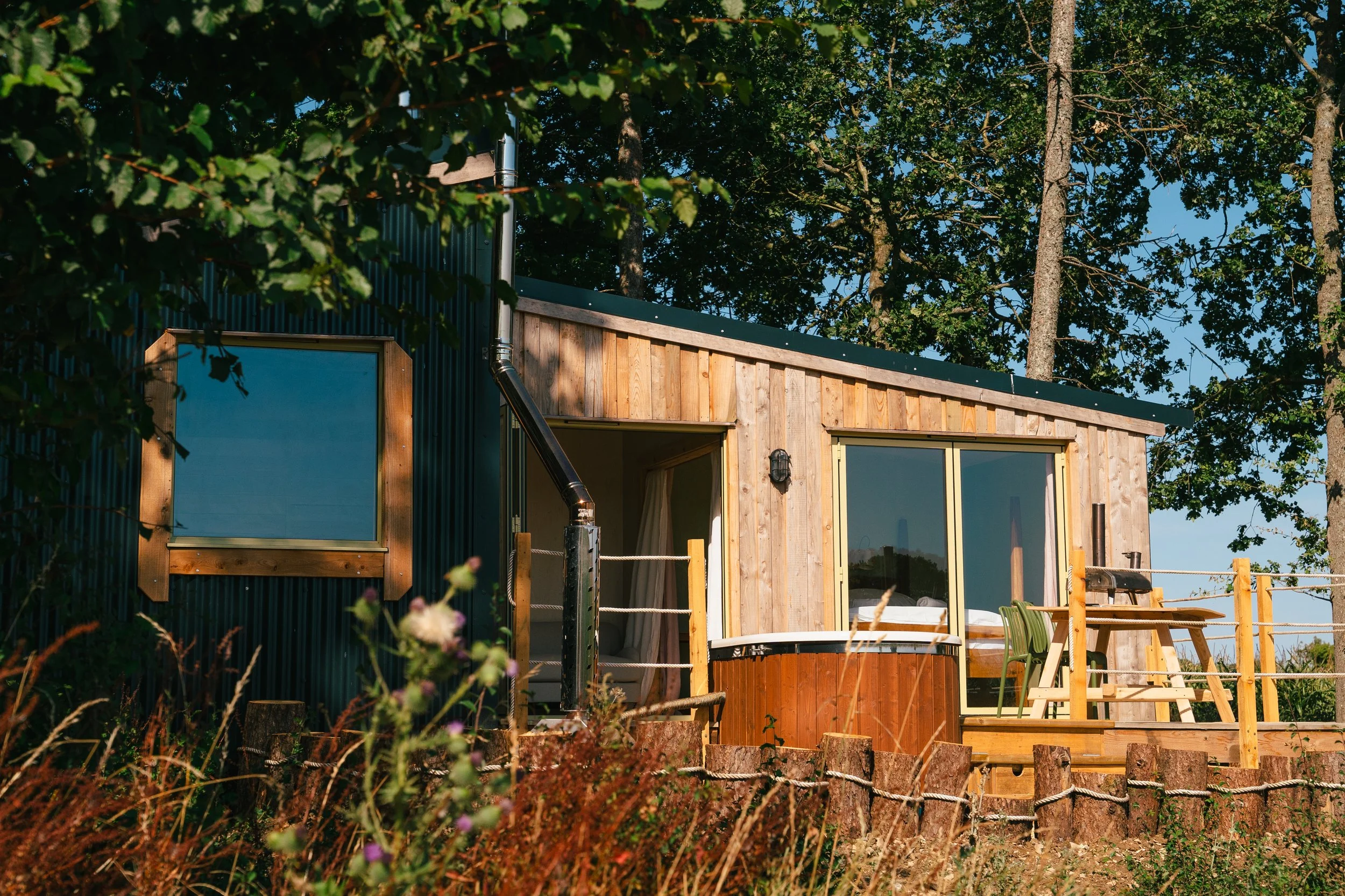 A woodland cabin in the Cotswolds surrounded by trees with green leaves, comfy beds, fresh linen, couples stay, glamping, king size,near a deck with outdoor furniture, a hot tub, luxury off grid stay. In Cotswolds village, Near Bibury and Cirencester