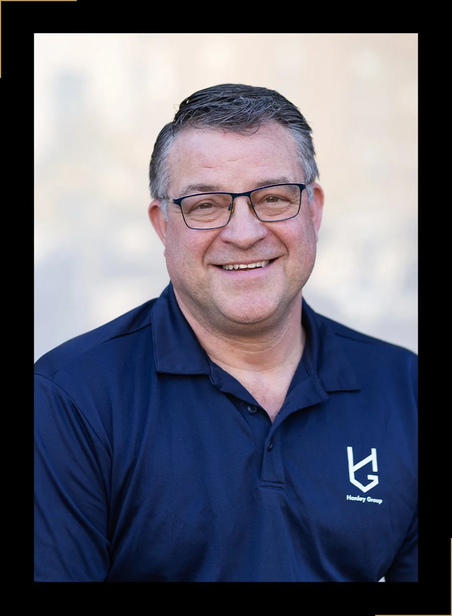 Portrait of Tim O'Donnell, a man with short dark hair, wearing glasses and a navy blue polo shirt with a Hanley Group logo, smiling directly at the camera.