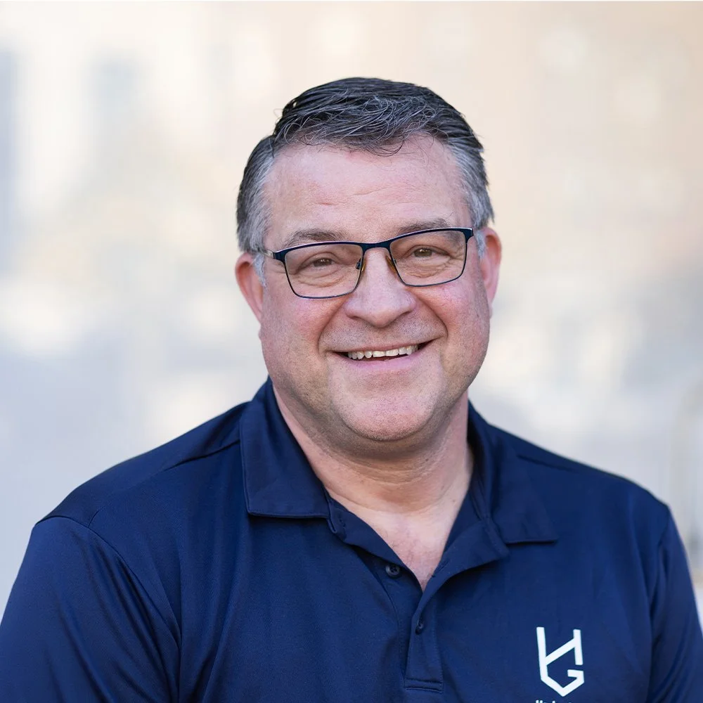 Portrait of Tim O'Donnell, a man with short dark hair, wearing glasses and a navy blue polo shirt with a Hanley Group logo, smiling directly at the camera.