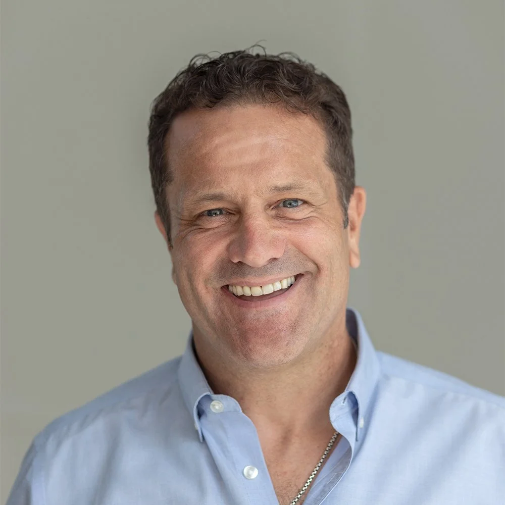 Headshot of Paudie Hanley, a professional man with short dark hair, wearing a light blue button-down shirt, looking directly at the camera with a friendly smile.