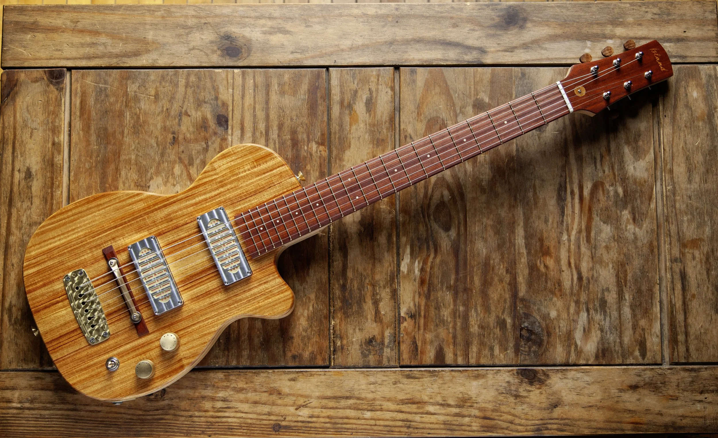 An electric Island Instruments guitar with a natural wood finish, resting on a wooden surface.