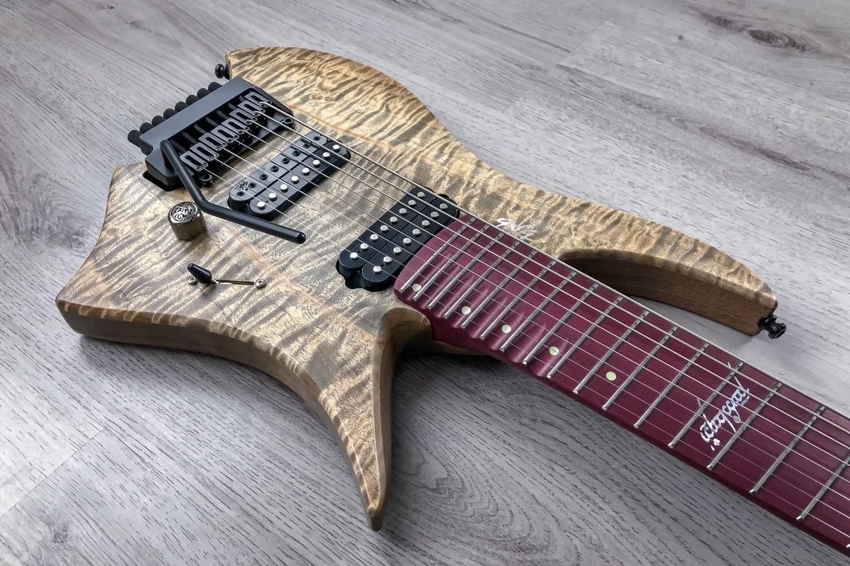 GNG Giulio Negrini guitar with a multiscale design, featuring a quilted maple top and a red fretboard, lying on a wooden floor.