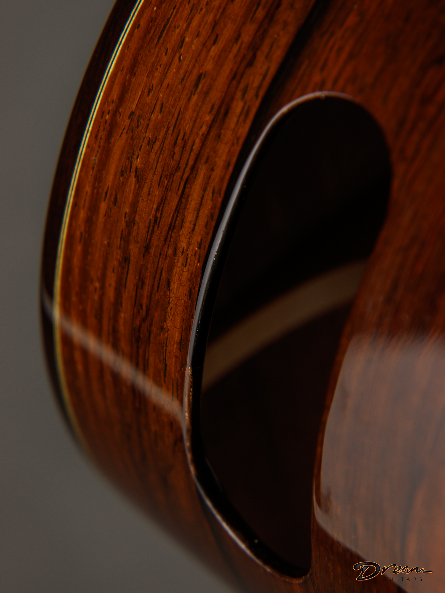 Close-up of the side of a wooden Laskin guitar with a sound hole, showing the wood grain and curved edges.
