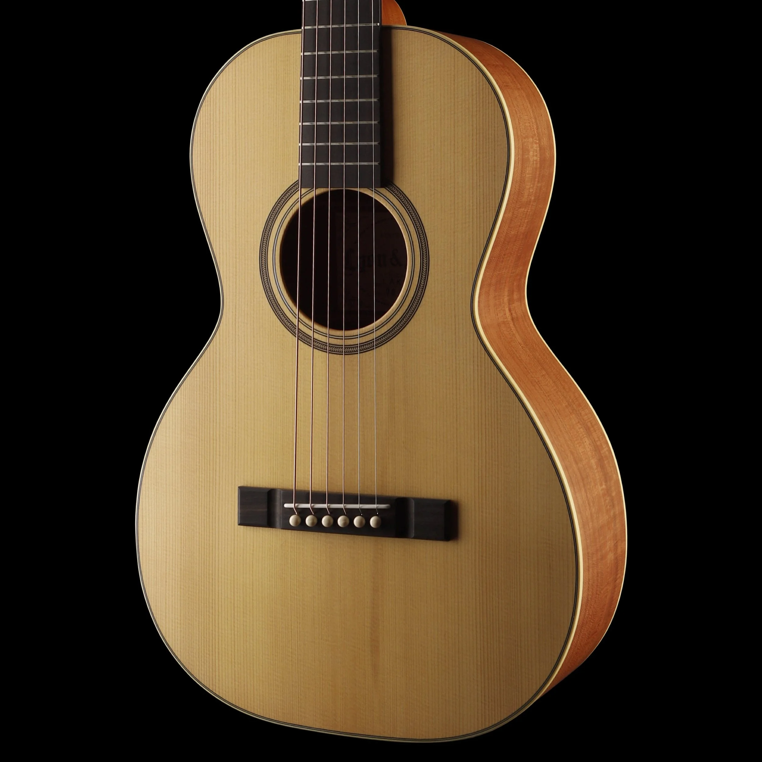 A close-up of an acoustic Lyon & Healy guitar with a light wood body, dark fretboard, strings, and sound hole against a black background.