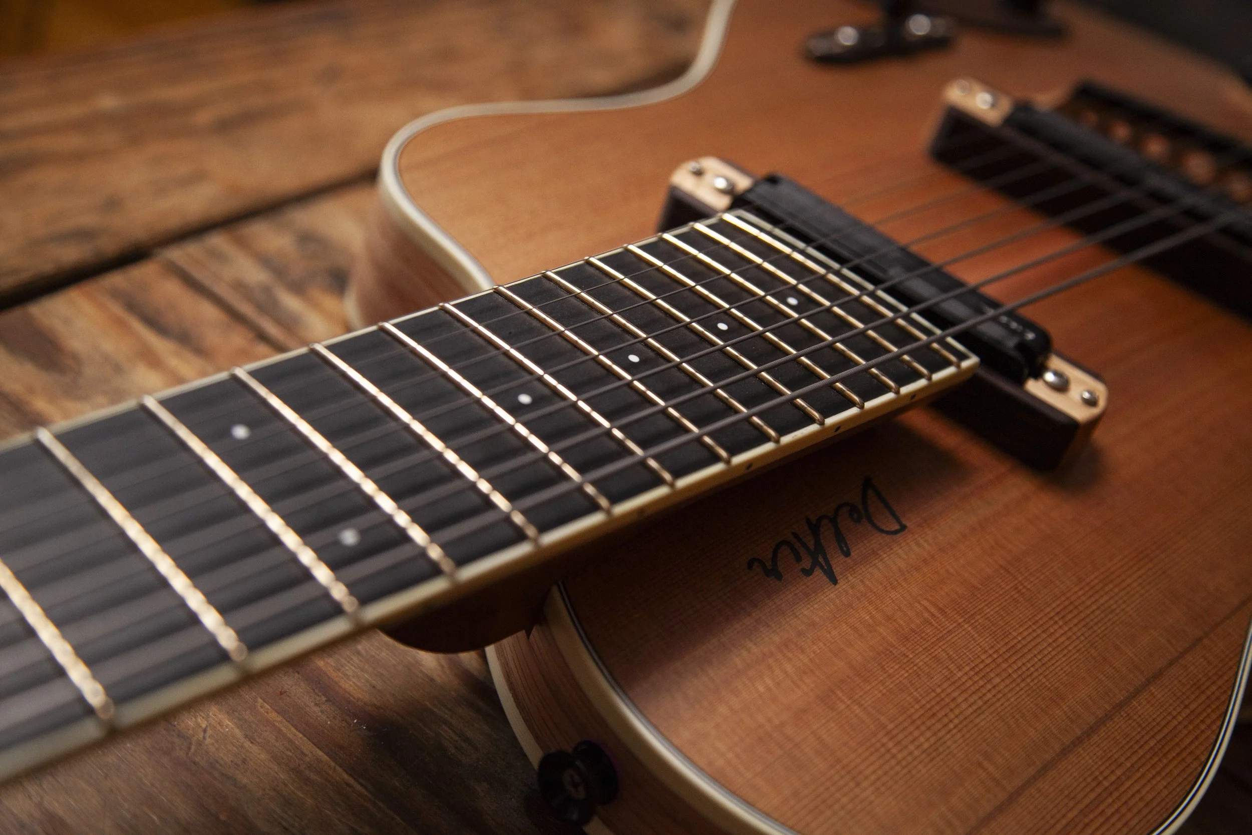 Close-up of an acoustic Island Instruments guitar placed on a wooden surface with a black electric pickup and strings in focus.