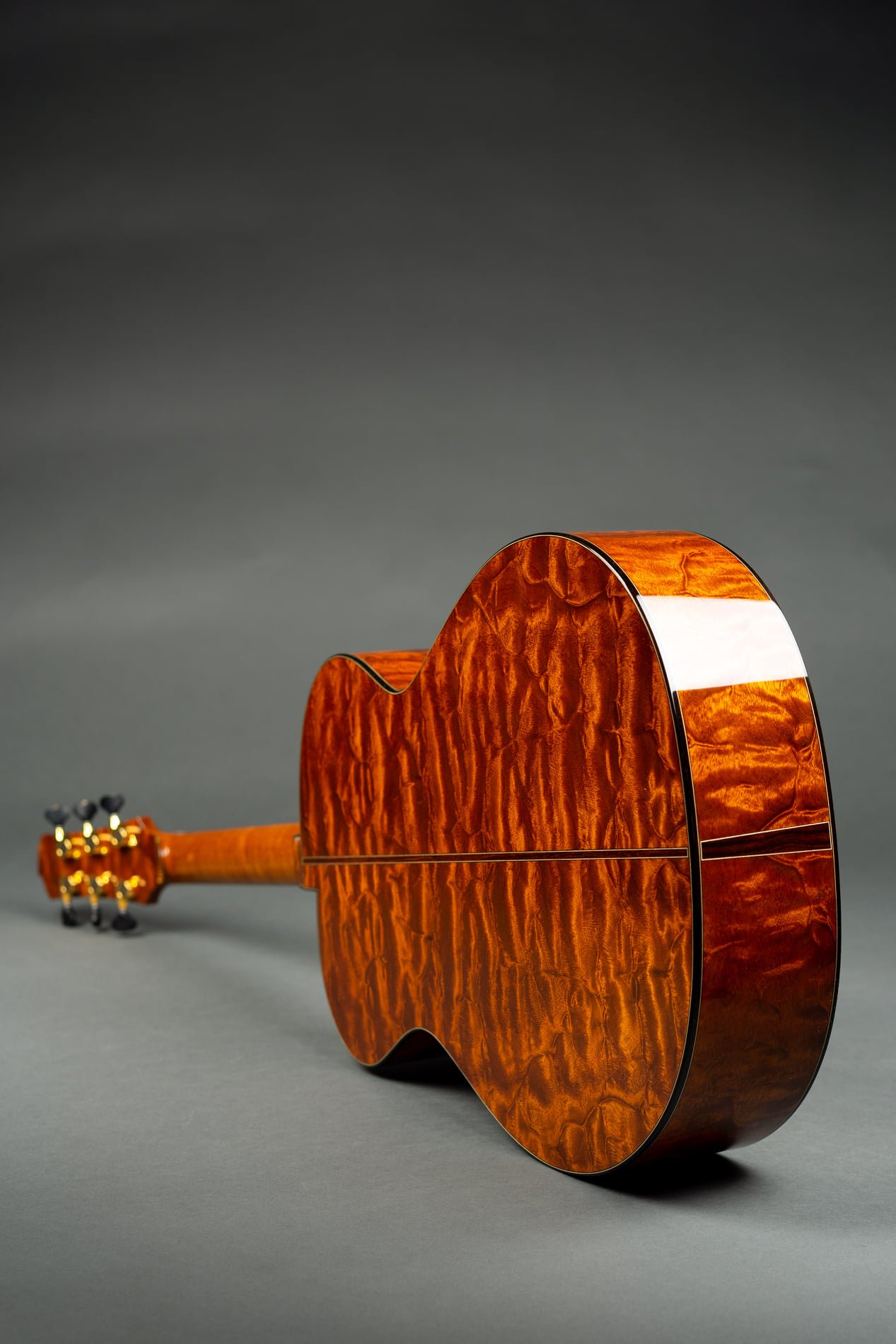A close-up of the back of an Isaac Jang acoustic guitar with a glossy, quilted wood finish, set against a dark gray background.