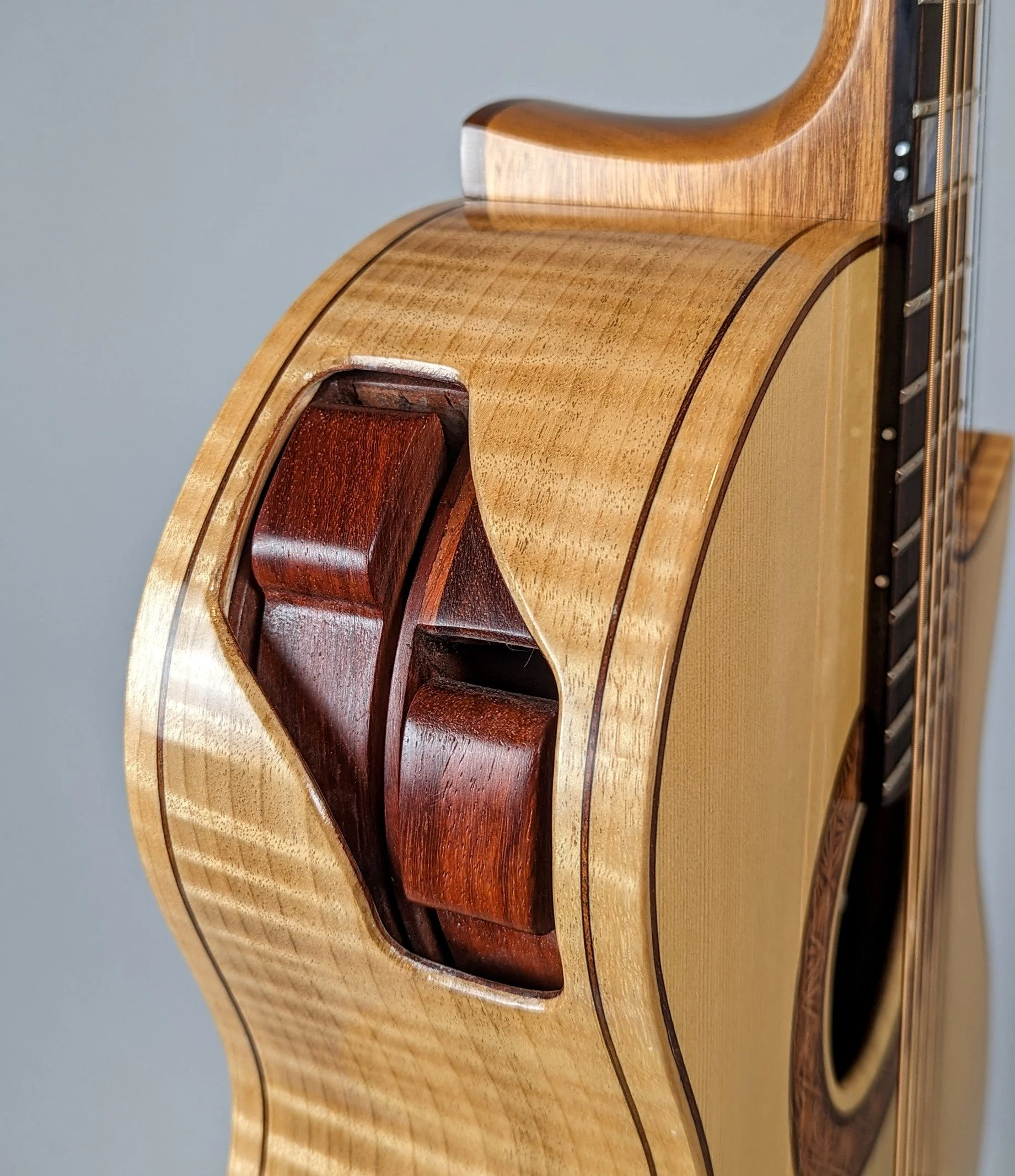 Close-up of the side of a Morgan Kelsey acoustic guitar showing the wooden body, pickguard, and tuning pegs.