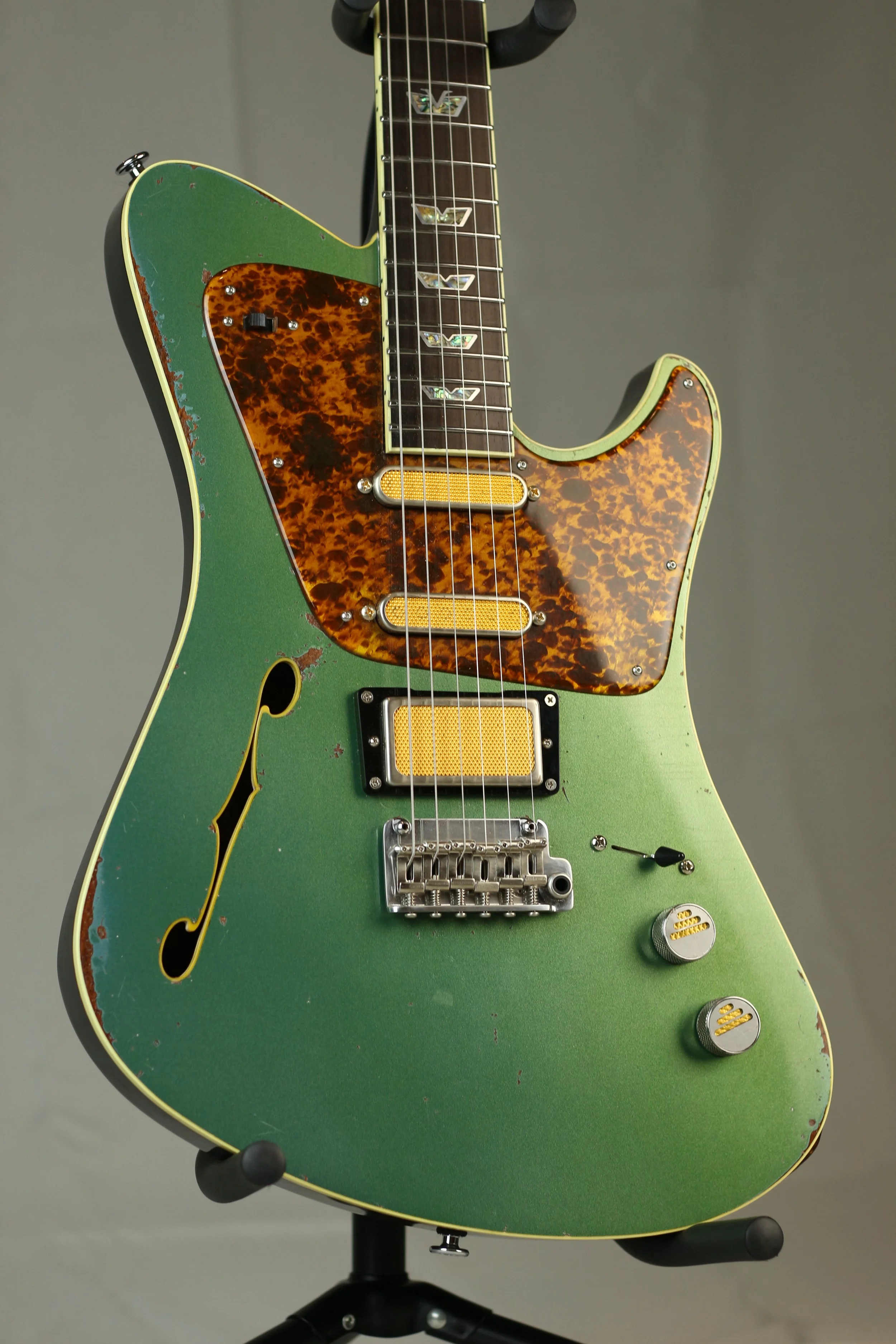 Vintage electric Corsell guitar with a worn green body, tortoiseshell pickguard, and gold pickups, resting on a black stand.