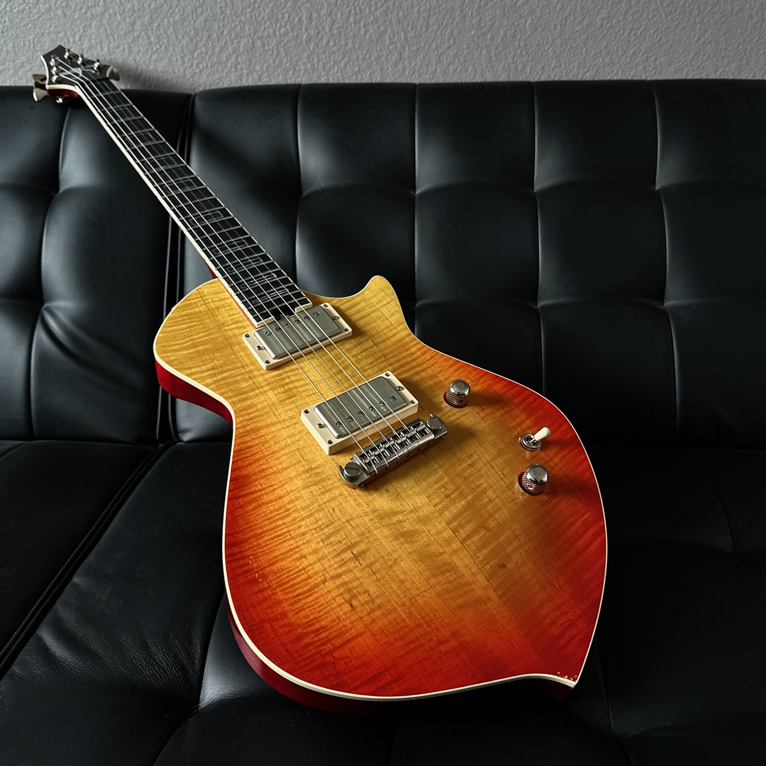 Electric Sully guitar with a sunburst finish resting on a black leather couch.