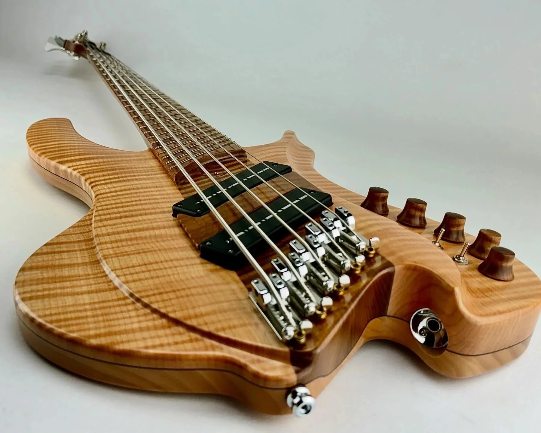 A close-up view of a wooden electric Torzal bass guitar lying on a white surface, showing the body, strings, pickups, and control knobs.