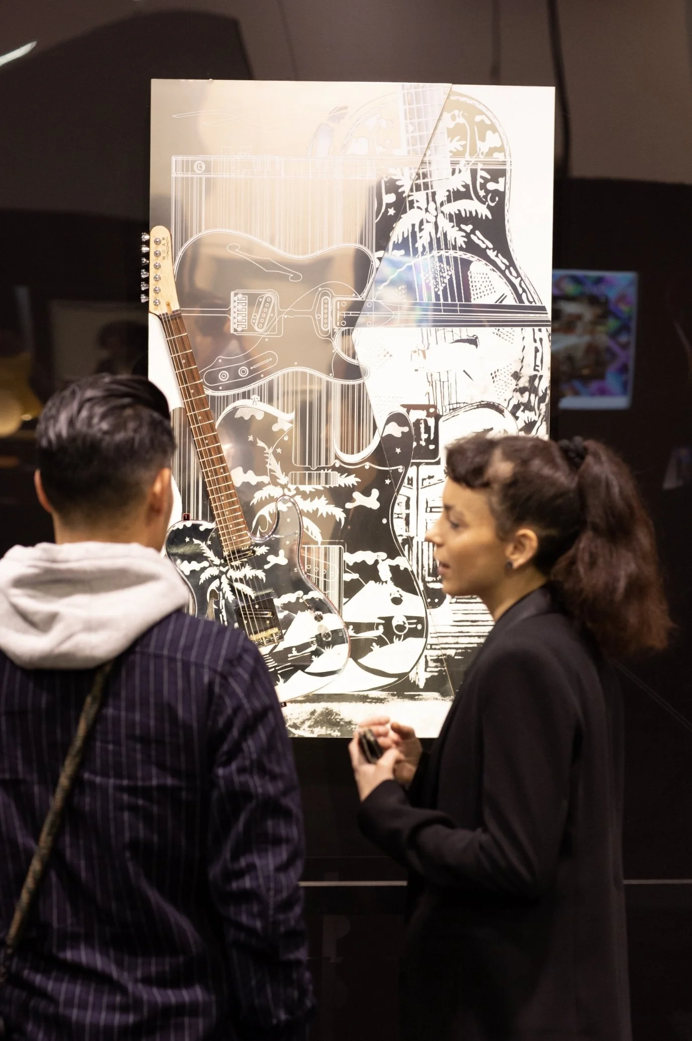 Two people viewing a guitar artwork featuring palm trees and abstract designs on aluminum.