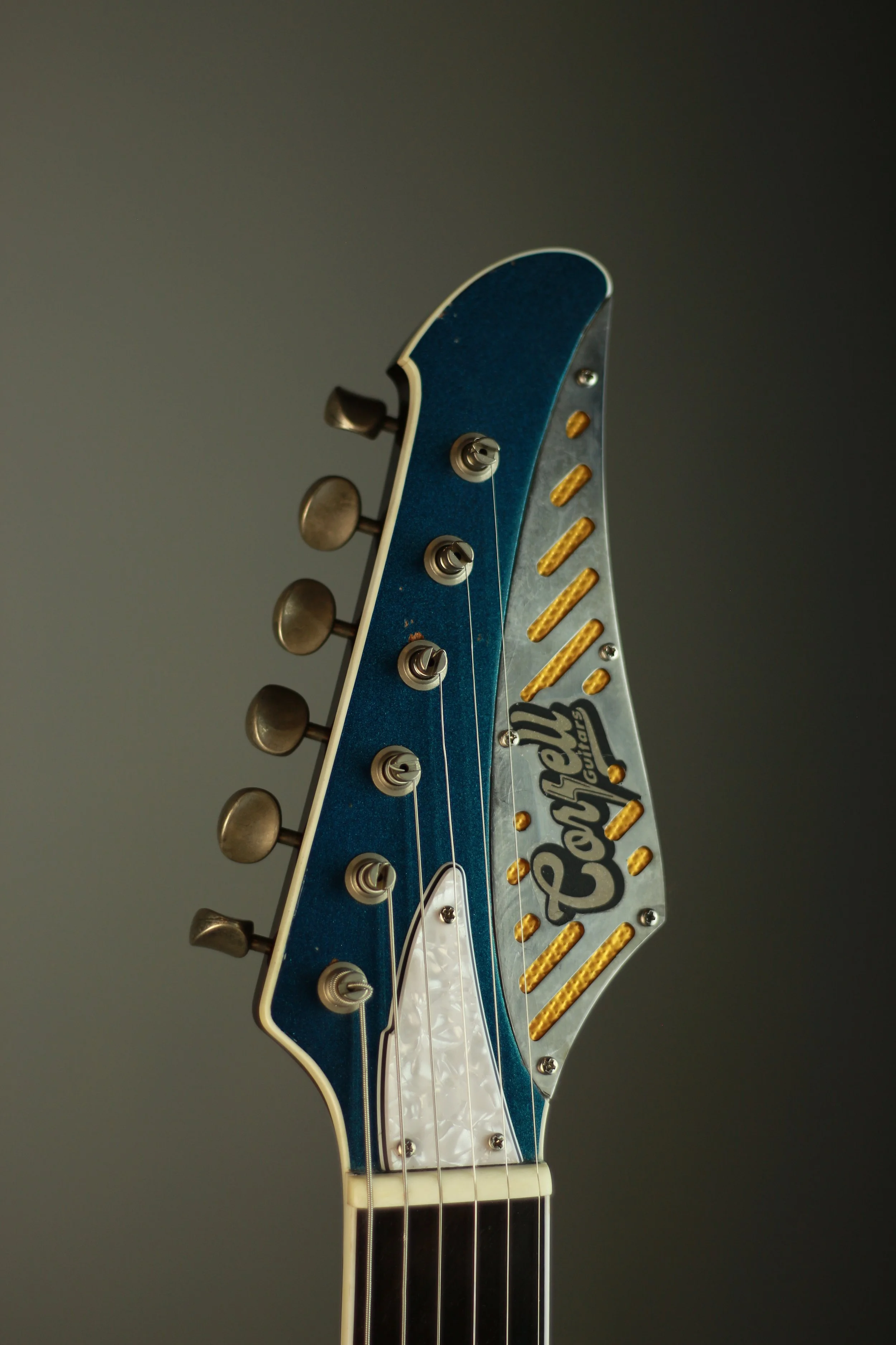 Close-up of a guitar headstock with tuning pegs and a custom metal logo plate reading 'Corsell' decorated with yellow accents.
