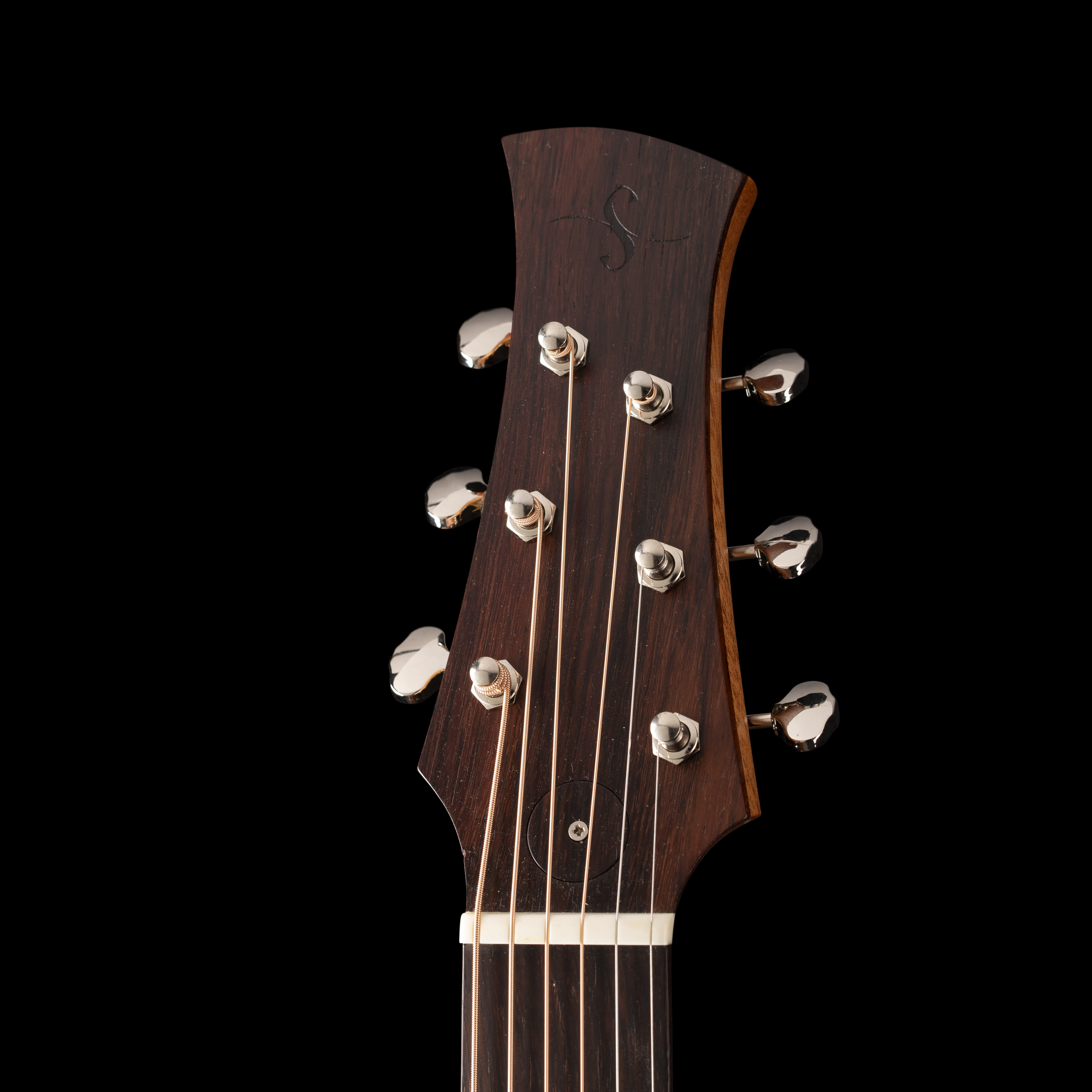 Close-up of the headstock of a wooden guitar with tuning pegs, strings, and a dark background.