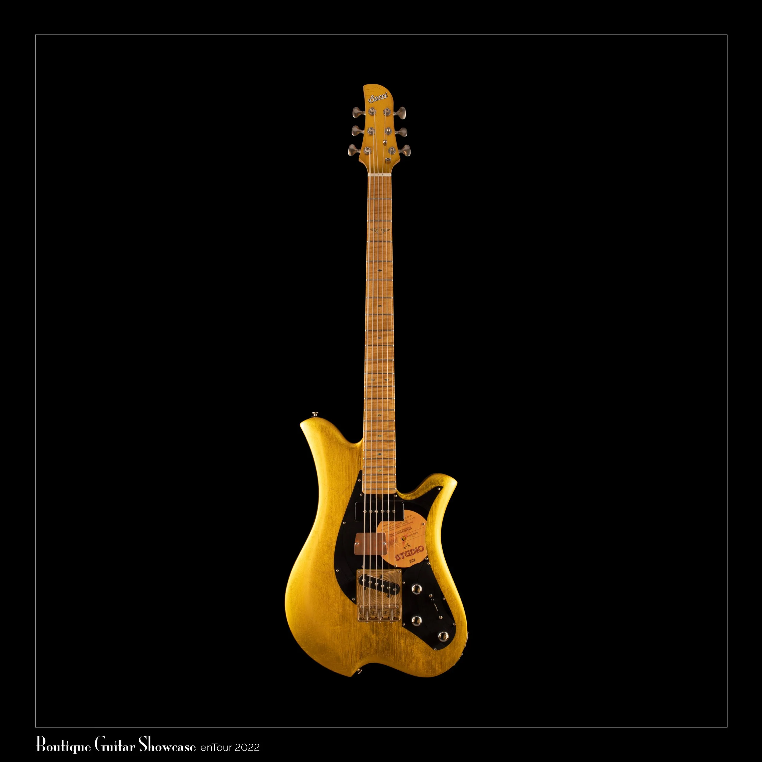 A golden Bacci Baritone electric guitar with a unique body shape against a black background.