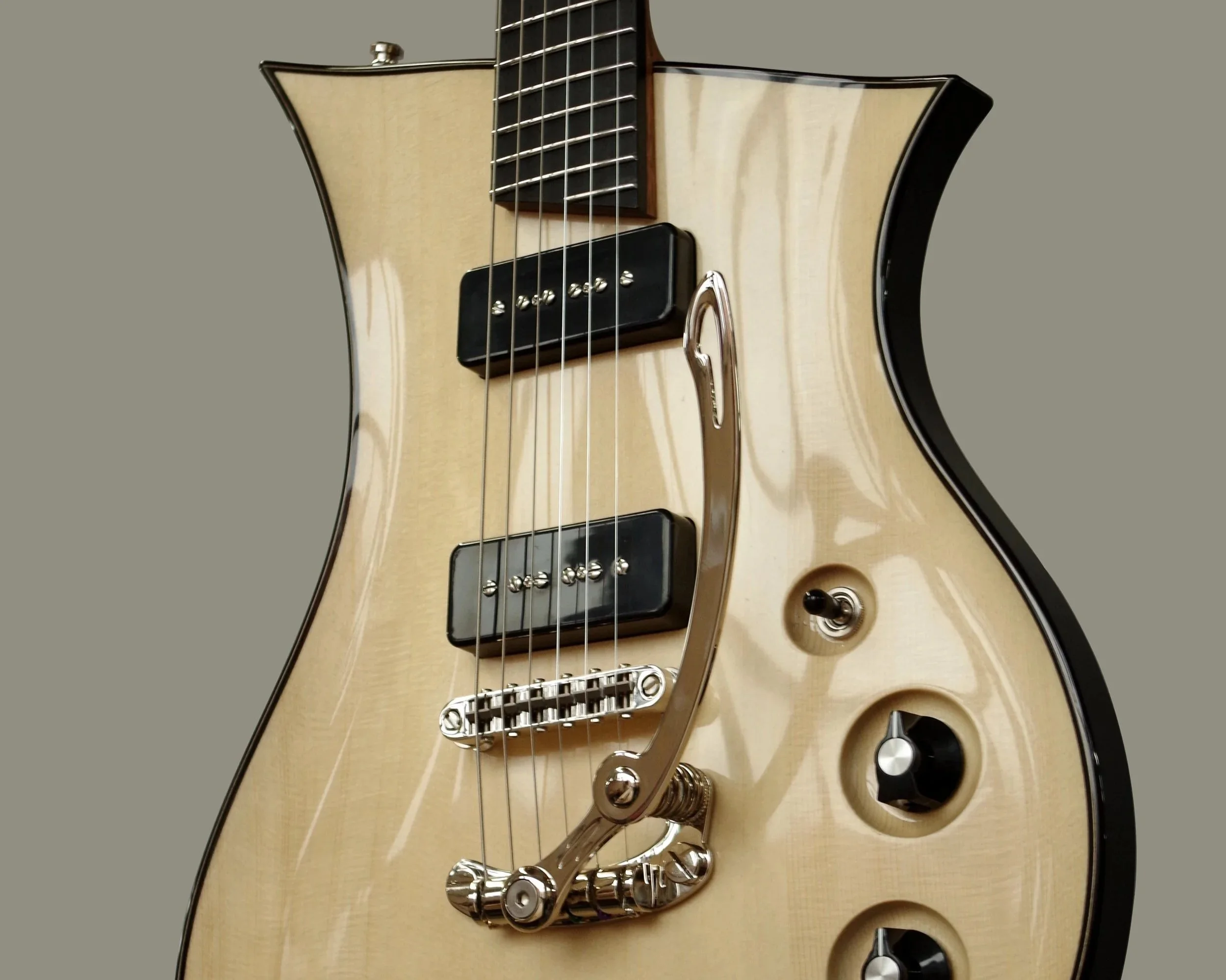 Close-up of a cream-colored electric Senez guitar with black accents, dual pickups, metallic tailpiece, and control knobs, against a neutral gray background.