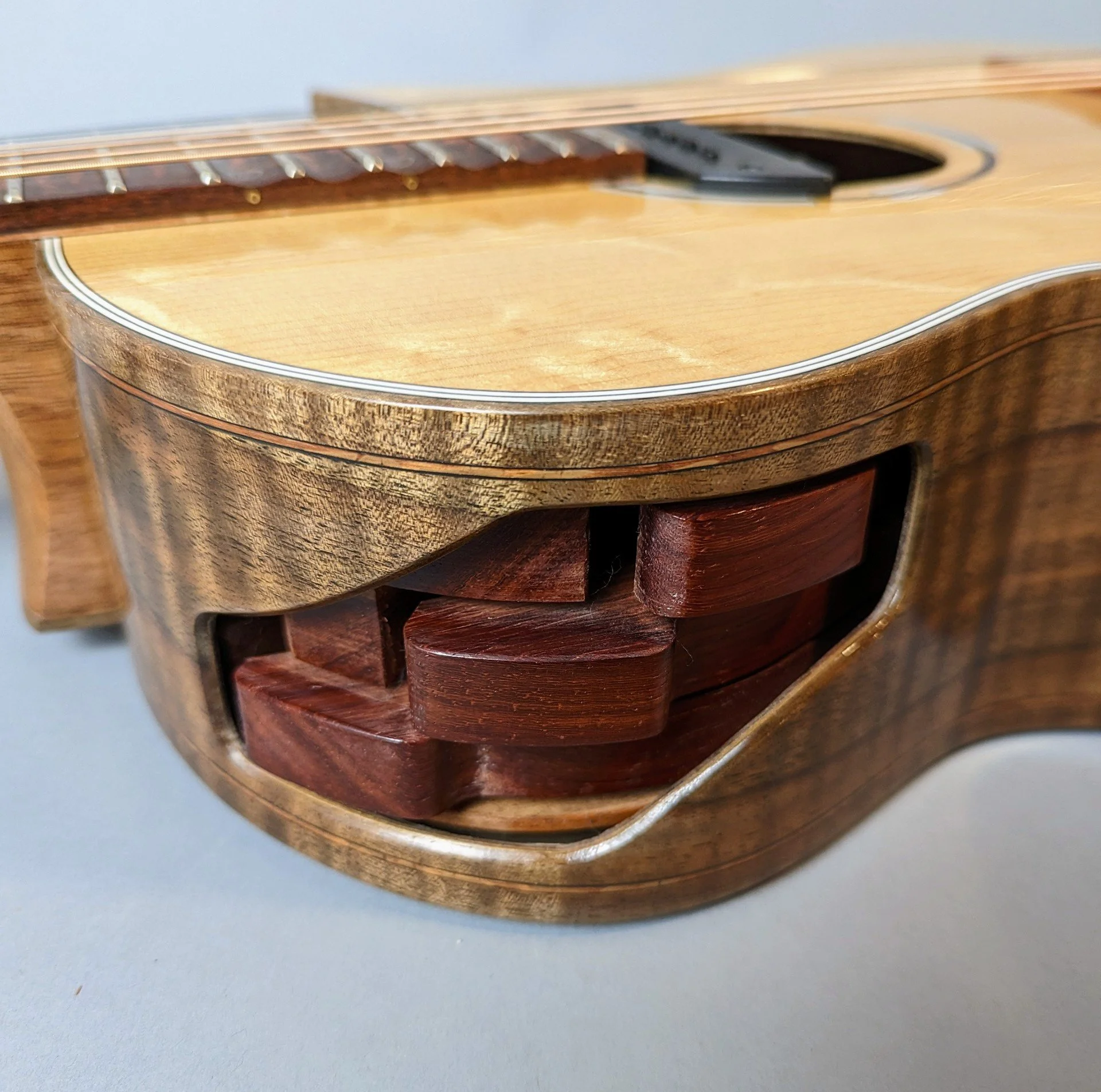 Close-up of a Morgan Kelsey acoustic guitar with a wooden case containing other guitar parts inside.