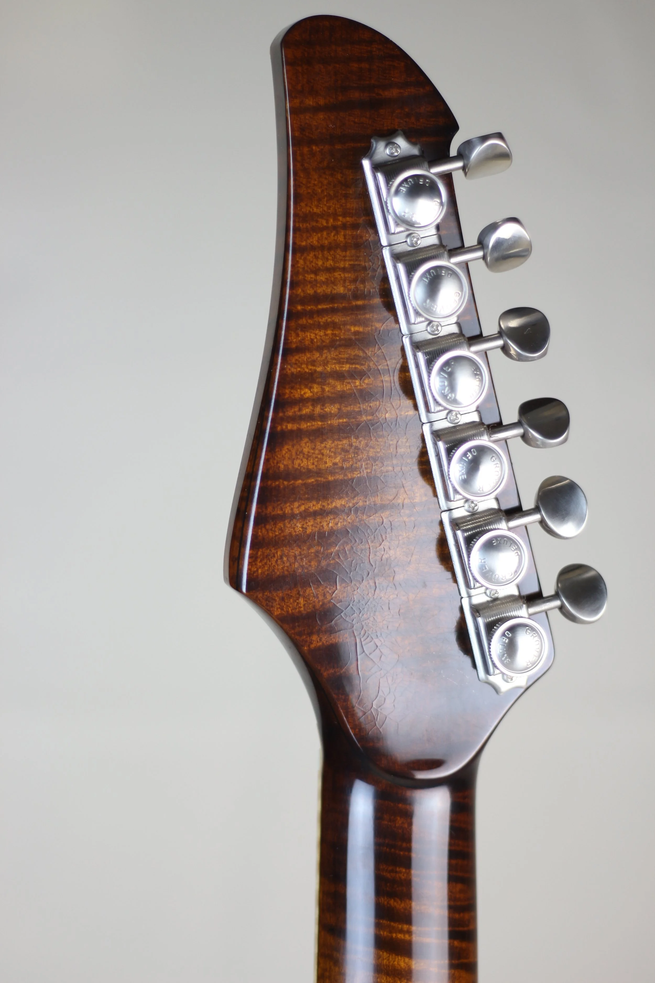 Close-up of a Corsell guitar headstock with six tuning pegs, made of dark, glossy wood with a figured pattern.