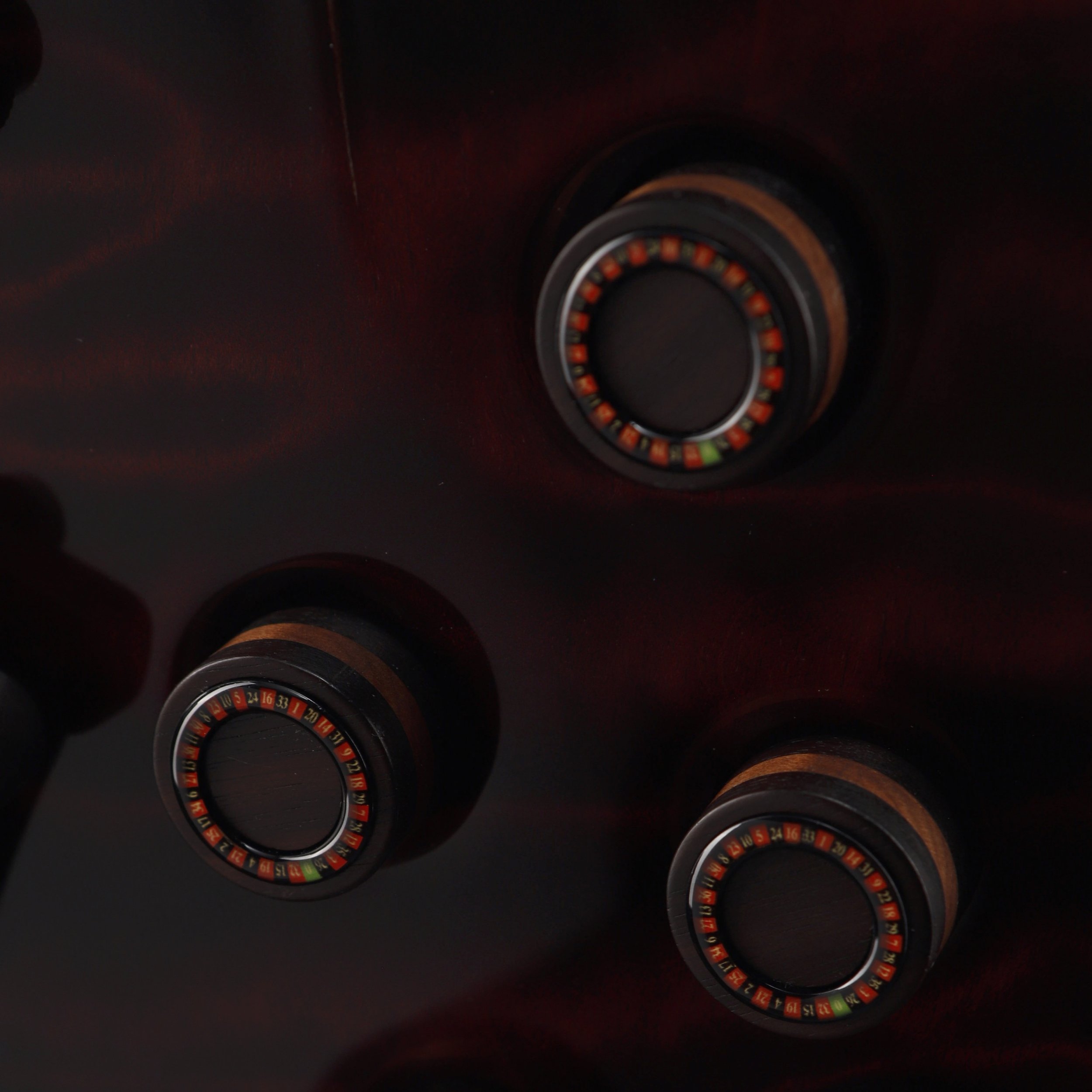 Close-up of three roulette wheels with black, red, green and gold accents on a dark wooden surface, Frank Hartung Guitar.