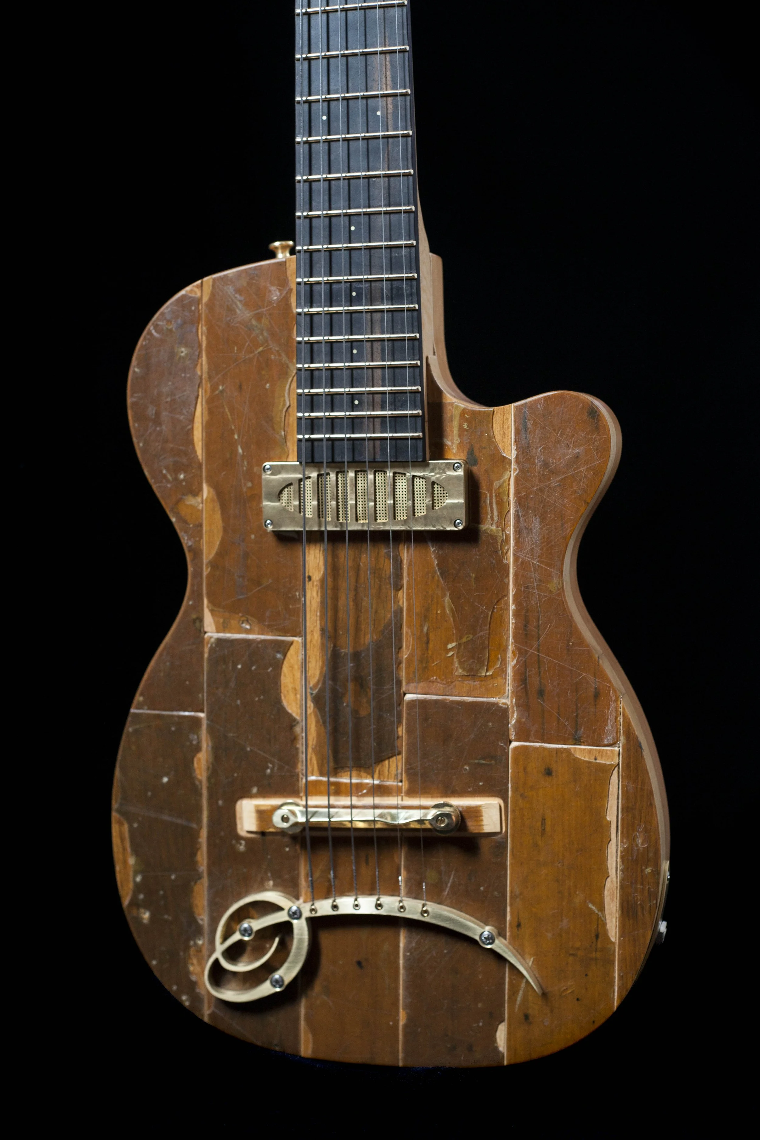 A vintage, distressed electric Island Instruments guitar with a worn wooden finish, visible scratches, and a unique design on the lower part, set against a black background.