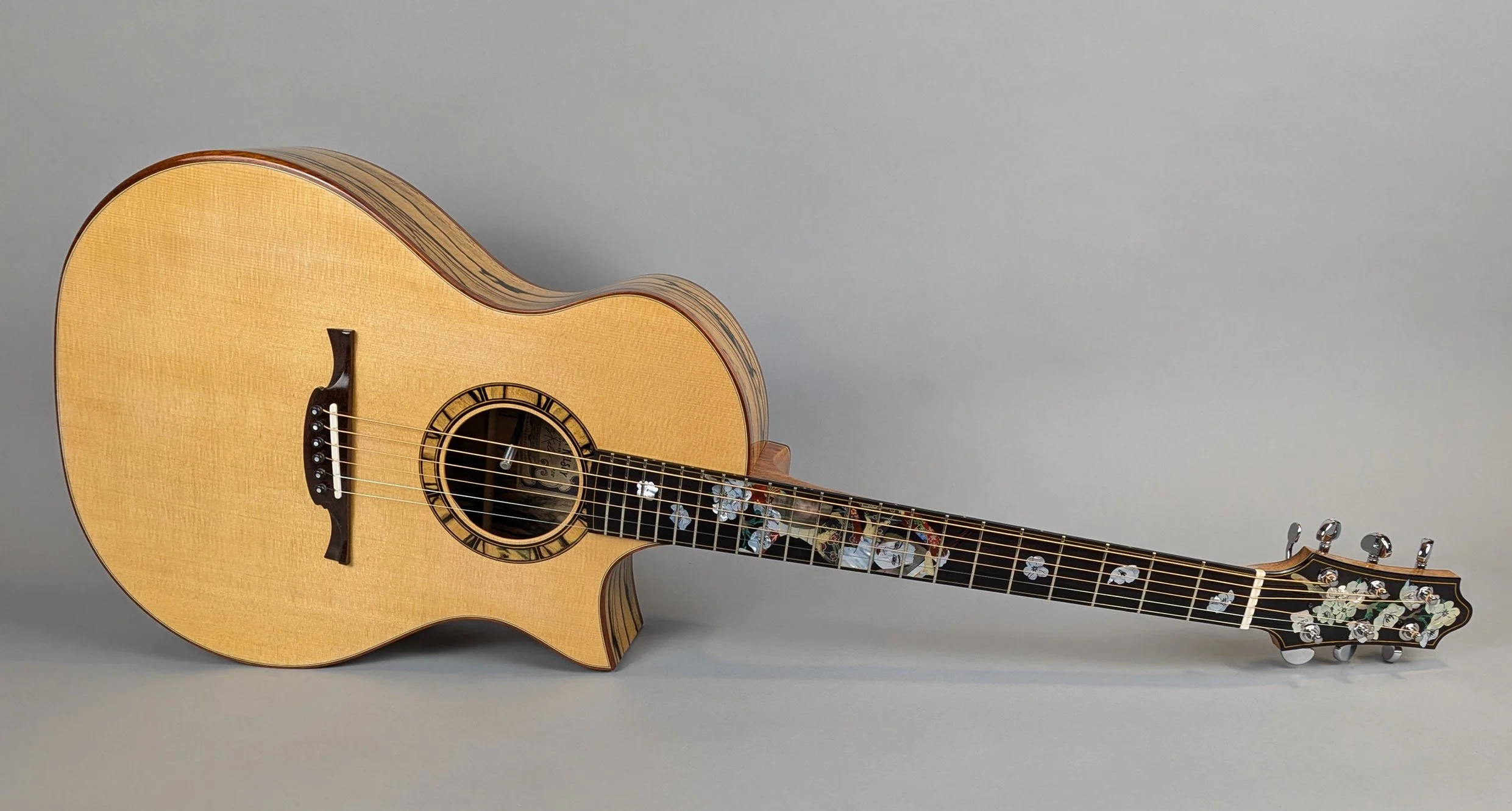A Morgan Kelsey acoustic guitar lying on its side against a plain gray background, with detailed inlays on the fretboard and decorative elements on the headstock.