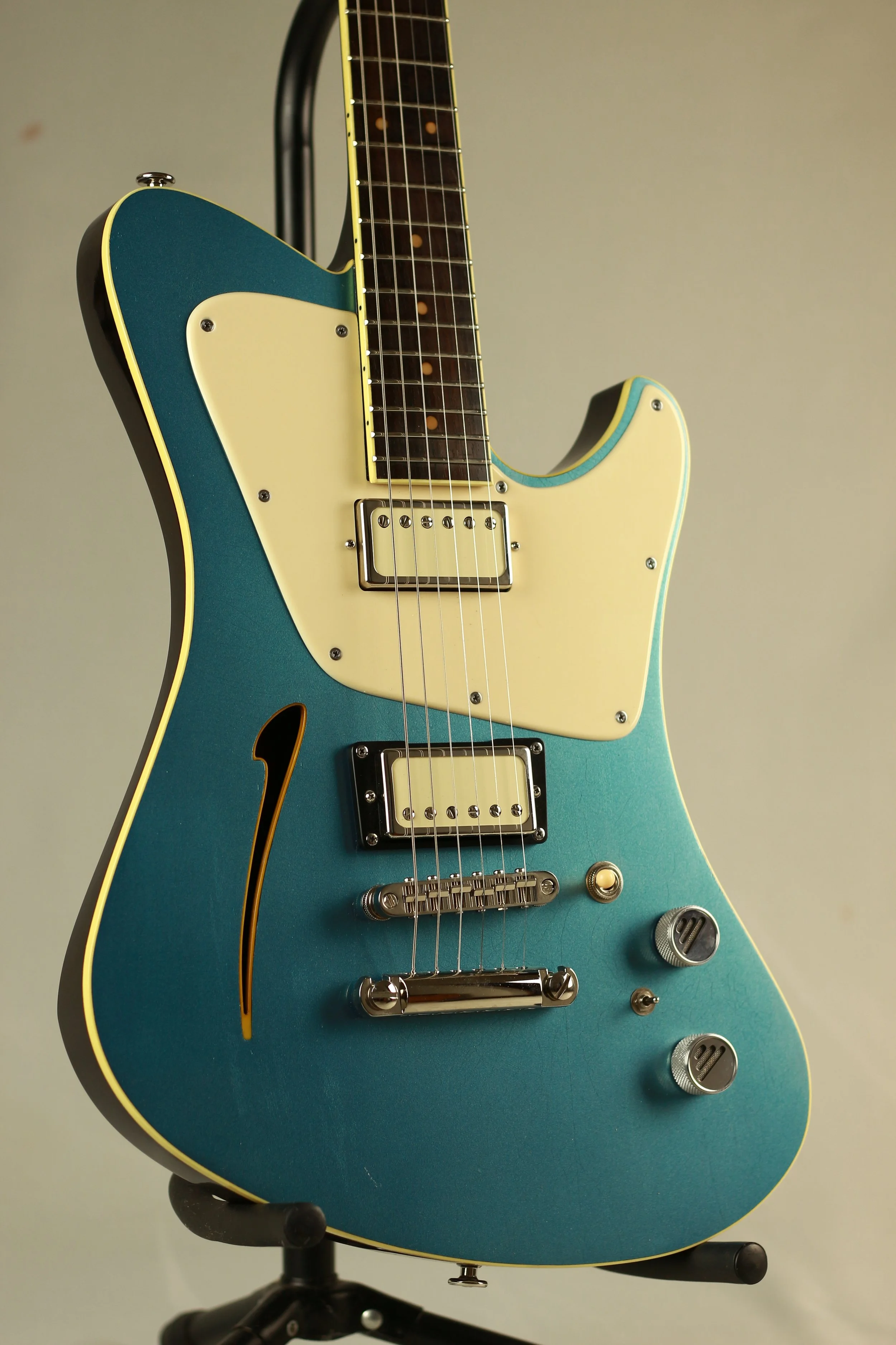 A close-up of a semi-acoustic Corsell electric guitar with a blue body, yellow pickguard, and silver hardware, resting on a black stand.