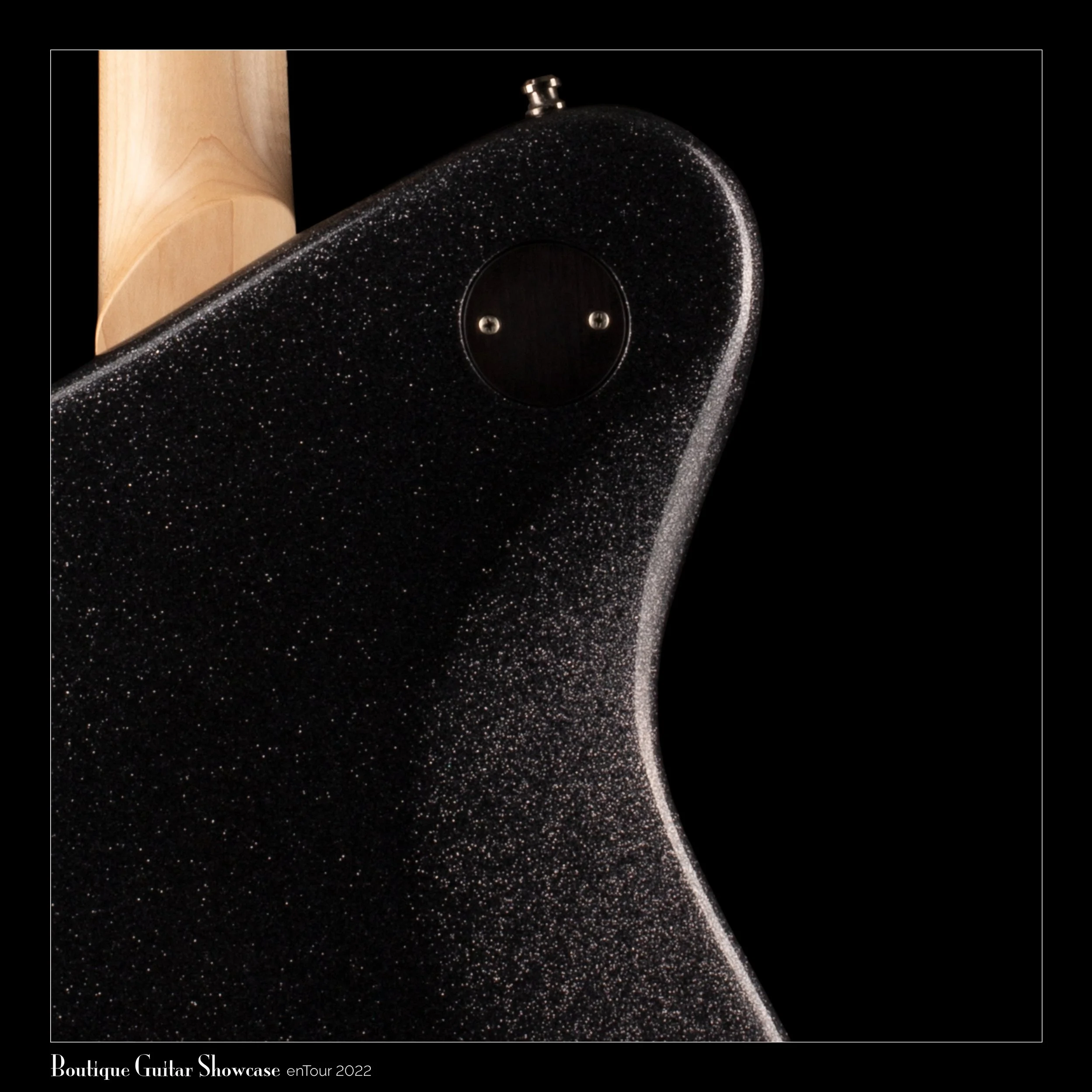 Close-up of a black Tausch guitar with a glittery finish and a natural wood neck against a black background, featuring a circular jack plate and the text 'Boutique Guitar Showcase enTour 2022'