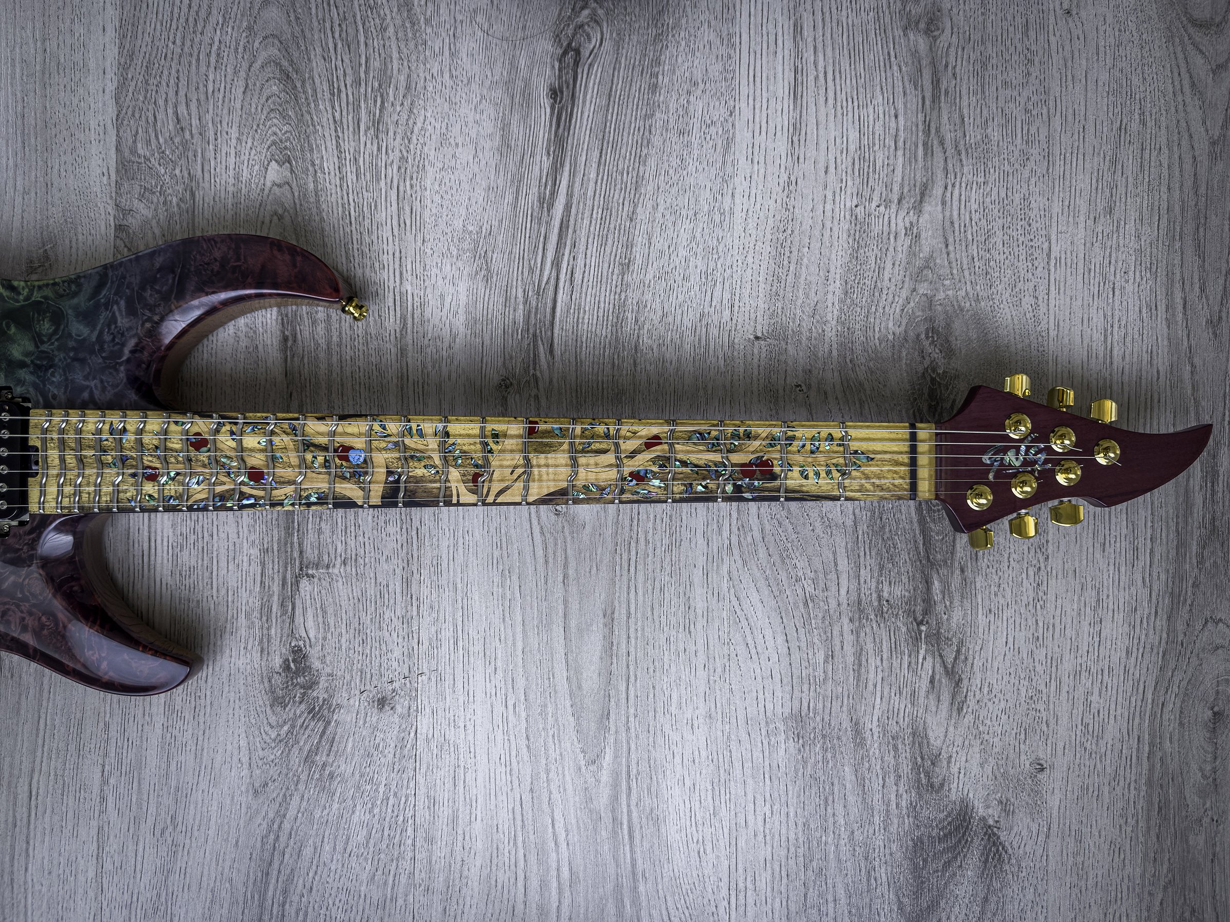 GNG Giulio Negrini electric guitar with a red marbled finish and a decorated wooden neck featuring a painted tree with colorful leaves, lying on a gray wooden floor.