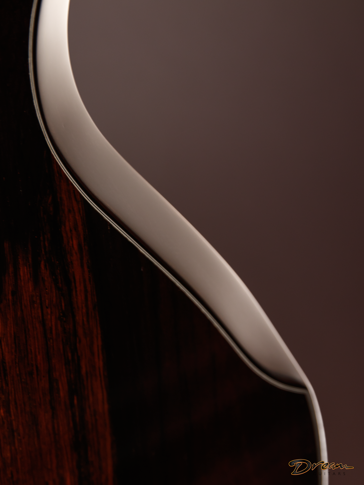 Close-up of an acoustic Laskin guitar's body, showing the wood grain and the edge of the soundboard with a white binding and a dark background.
