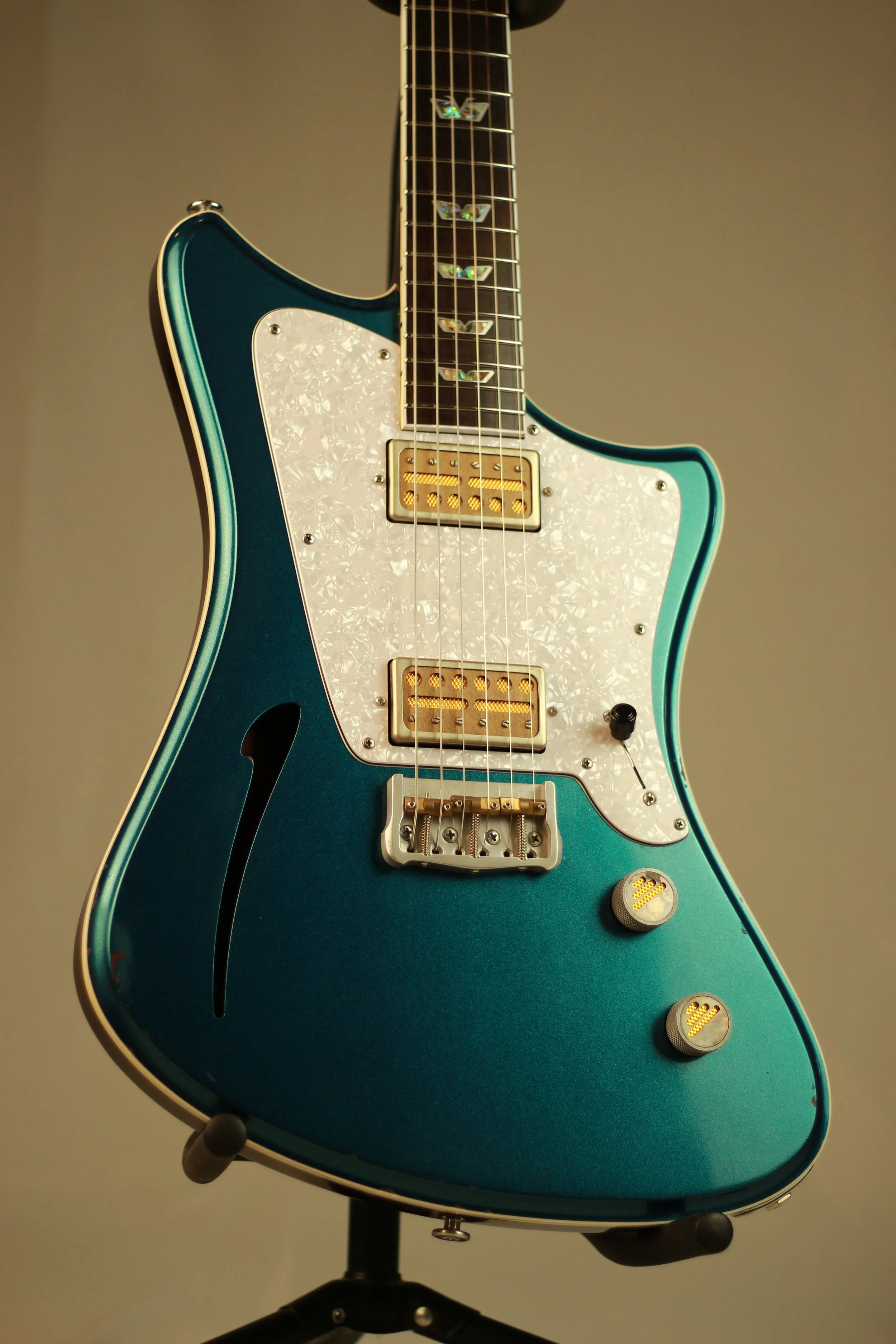 A teal electric Corsell guitar with a white pearloid pickguard, gold pickups, and control knobs, displayed on a black stand against a plain background.