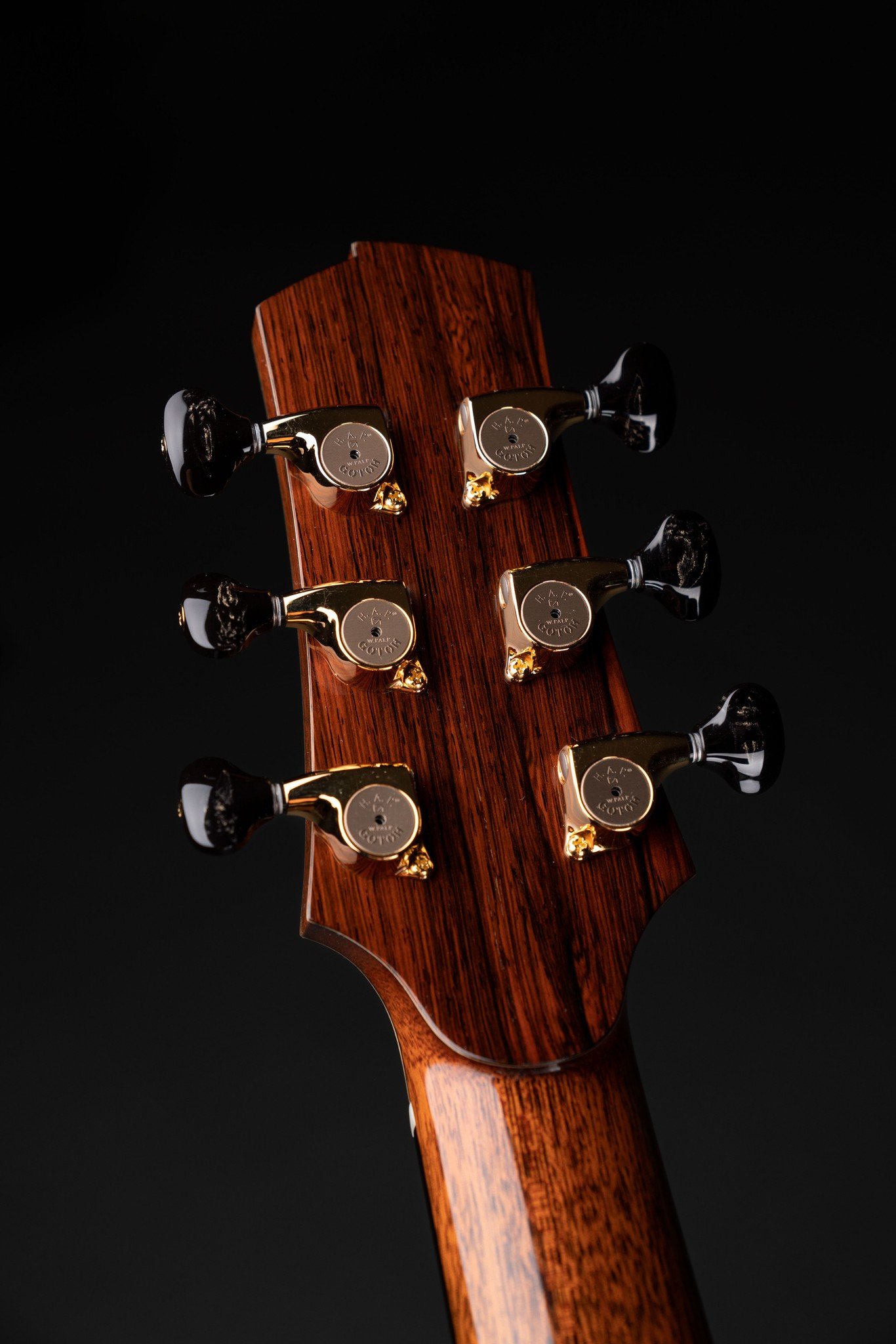 Close-up of the headstock of an Isaac Jang acoustic guitar with gold tuning pegs against a black background.