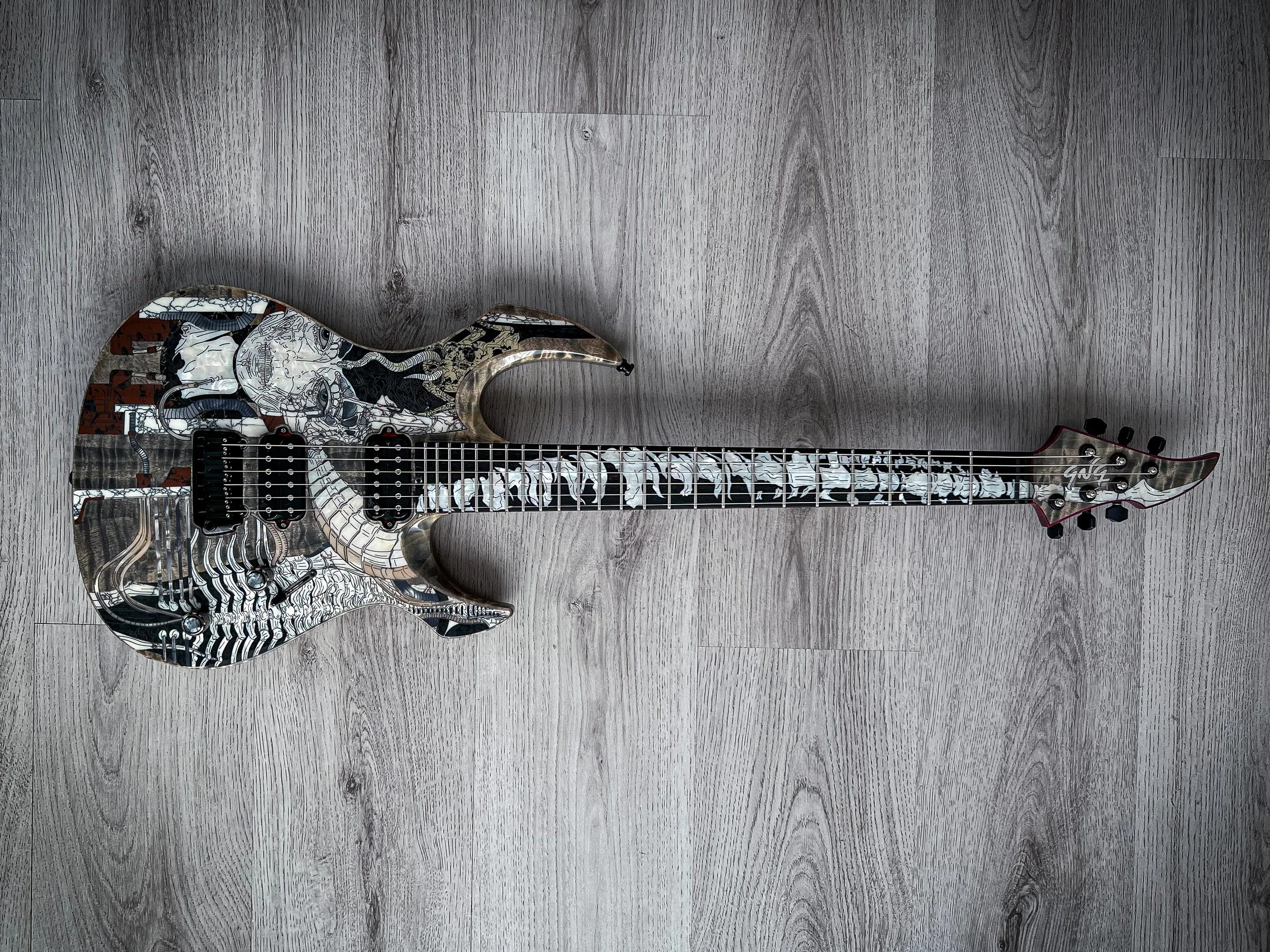 GNG Giulio Negrini electric guitar with a black and white abstract artwork design, featuring intricate patterns and images, lying on a wooden floor.