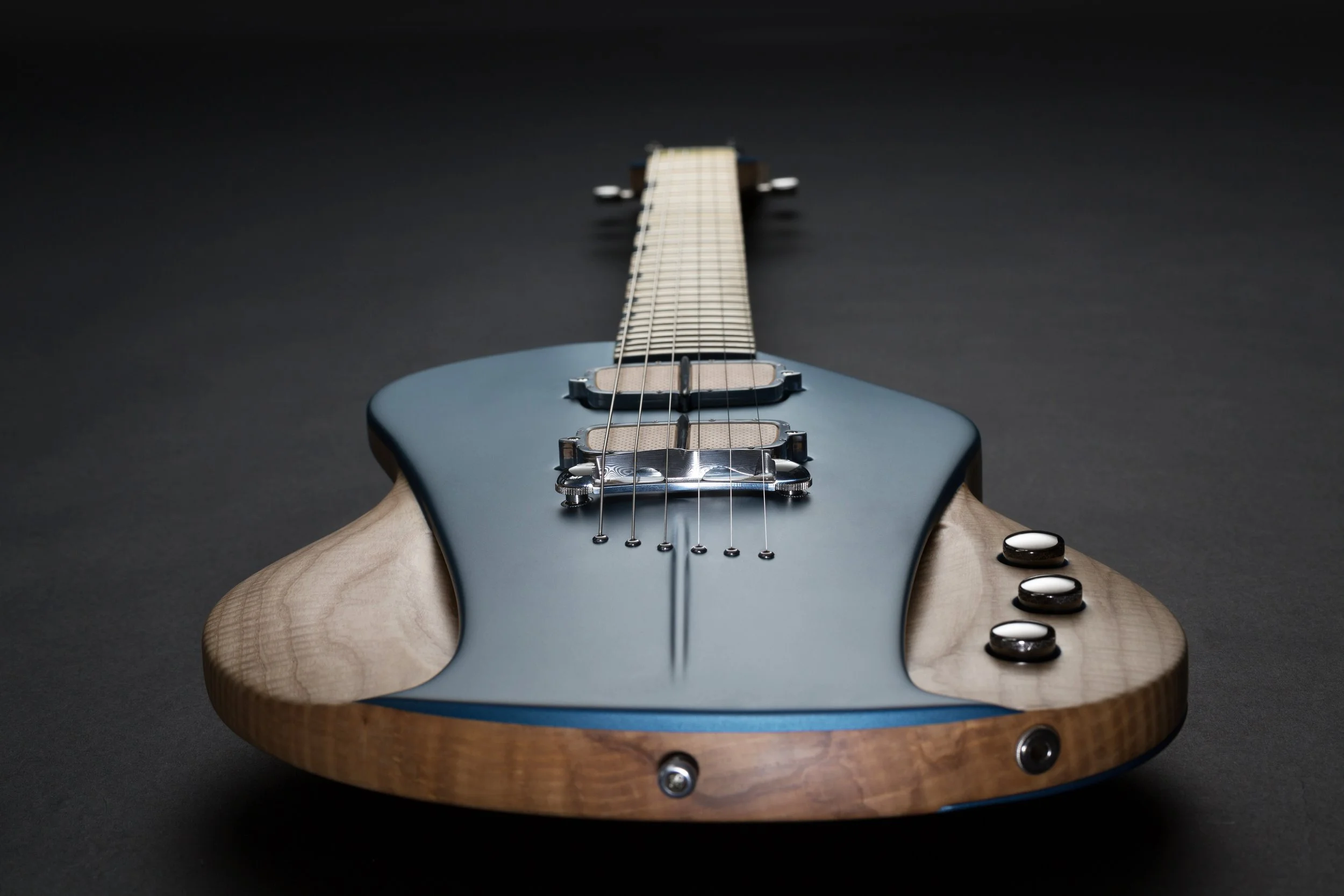 Electric Sauvage guitar with a blue body, wooden sides, and black and white controls, placed on a dark surface.