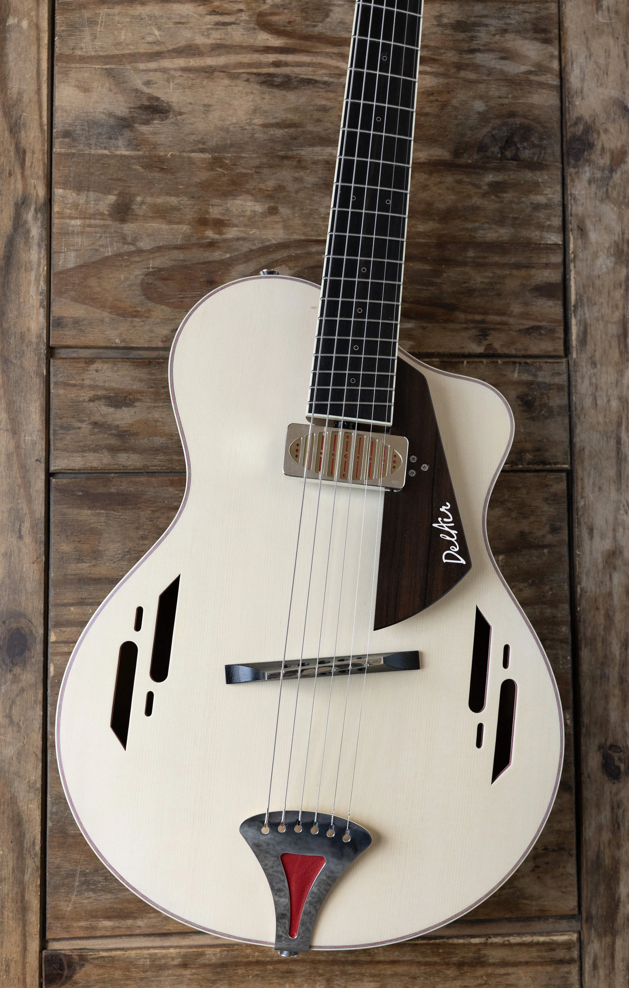 Cream-colored electric Island Instruments guitar with black pickguard, die-cast bridge, and intricate cut-out designs on the body, resting on a wooden surface.