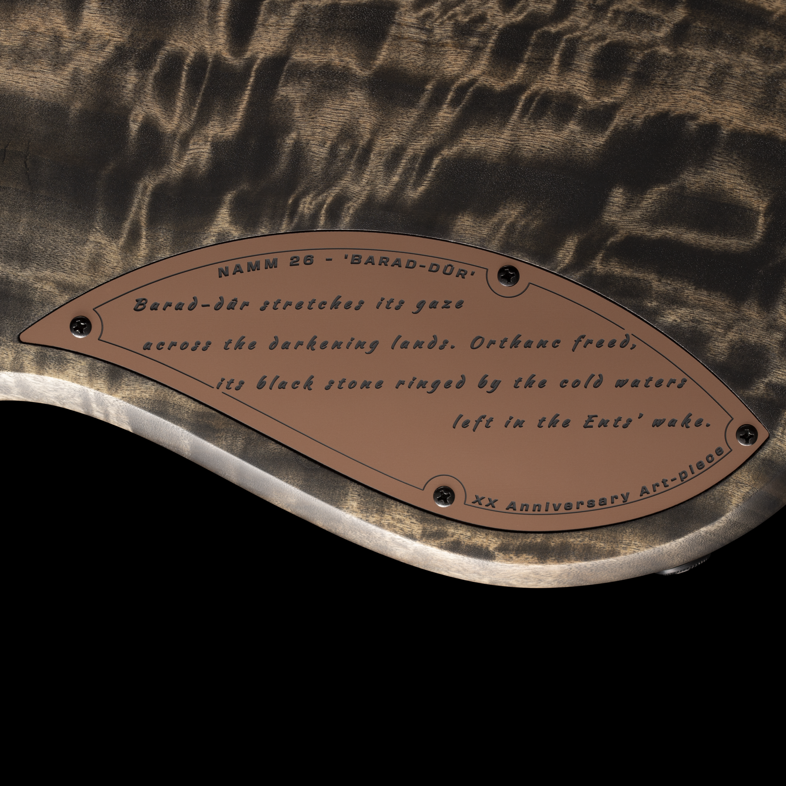 Close-up of a wooden object with a metallic plaque engraved with text, including 'NAMM 26 - 'BARAD-DÛR' and other words in a decorative script. The wood has a dark, textured grain with a glossy finish, and the plaque is attached with small screws.GNG