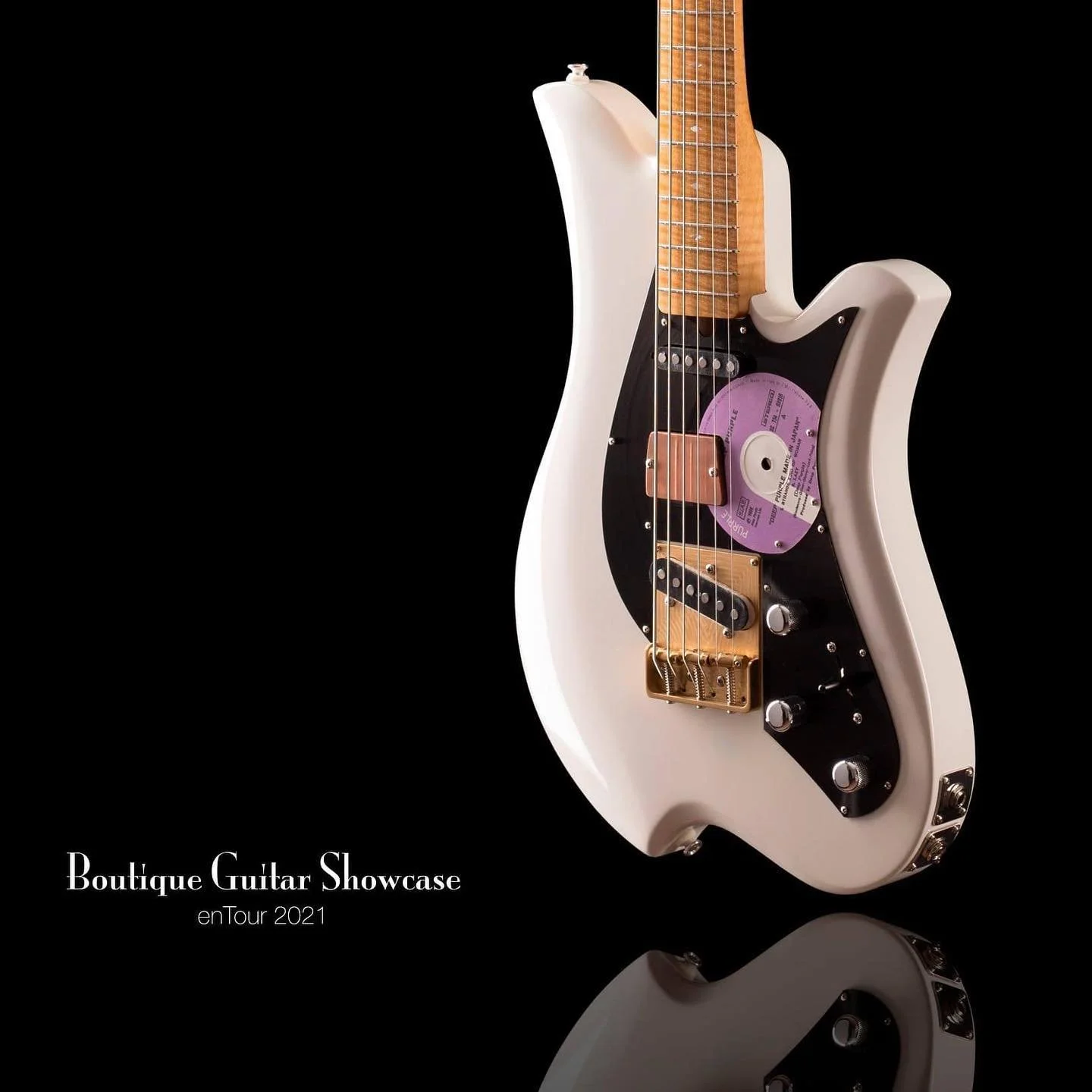White Bacci Baritone electric guitar with a unique design featuring a vinyl record as part of the body, displayed against a black background with text "Boutique Guitar Showcase enTour 2021."