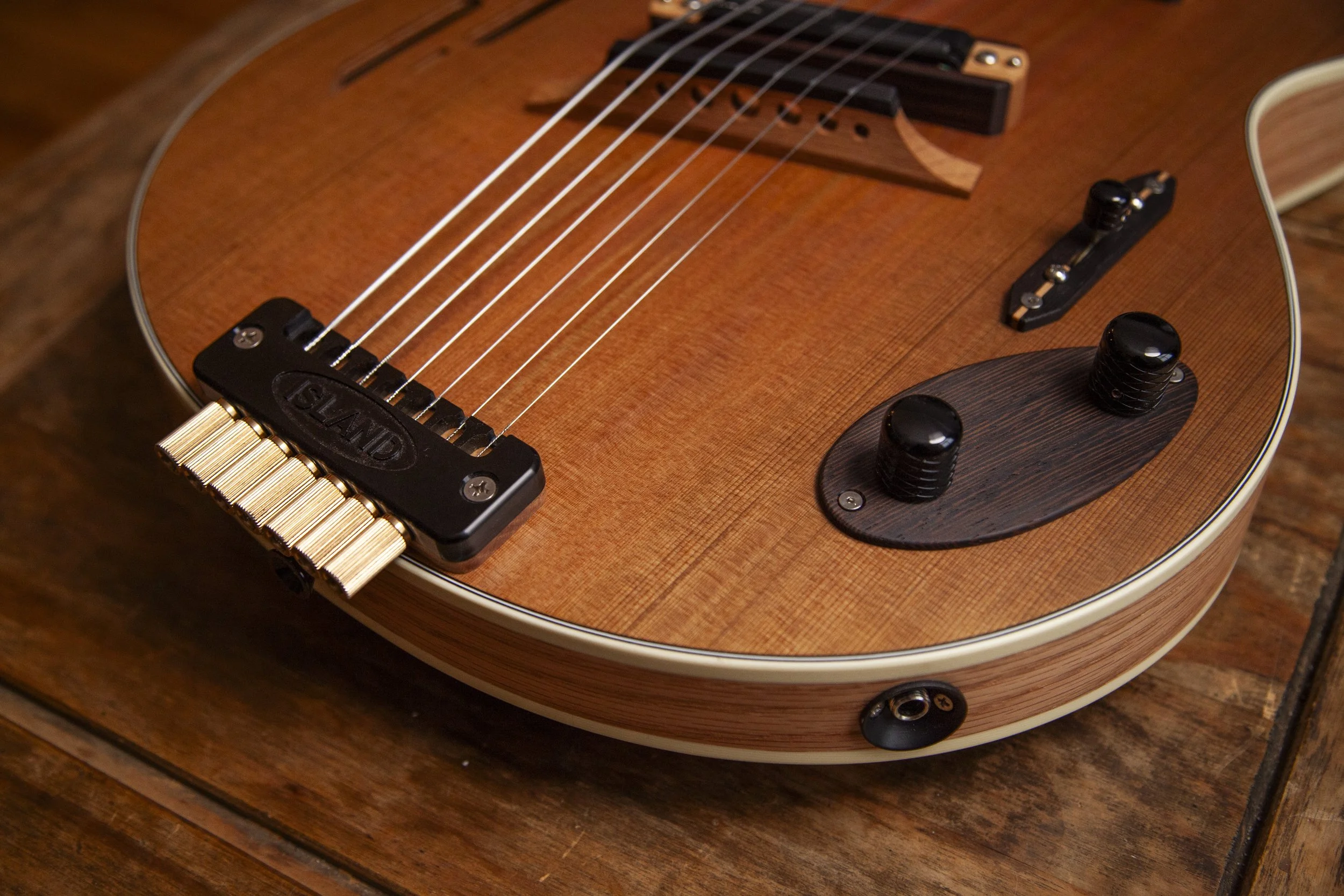 Close-up of an acoustic Island Instruments guitar's body, strings, bridge, and control knobs on a wooden surface.