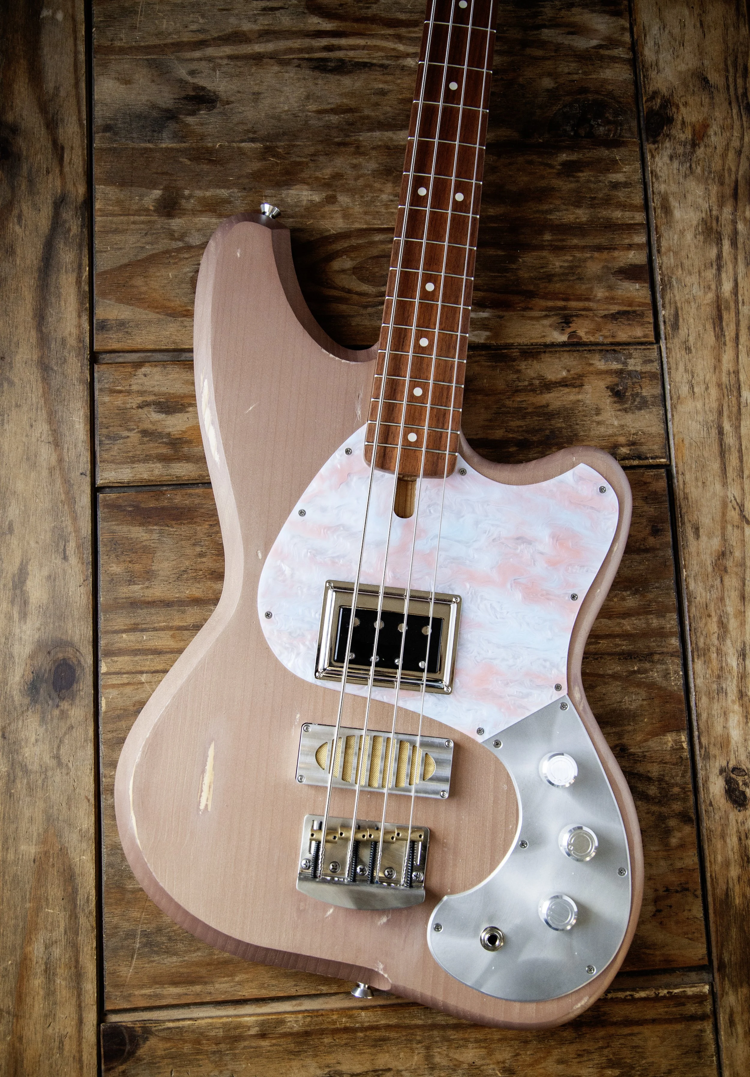 A pink electric Island Instruments guitar with a white pearl pickguard resting on a wooden surface.