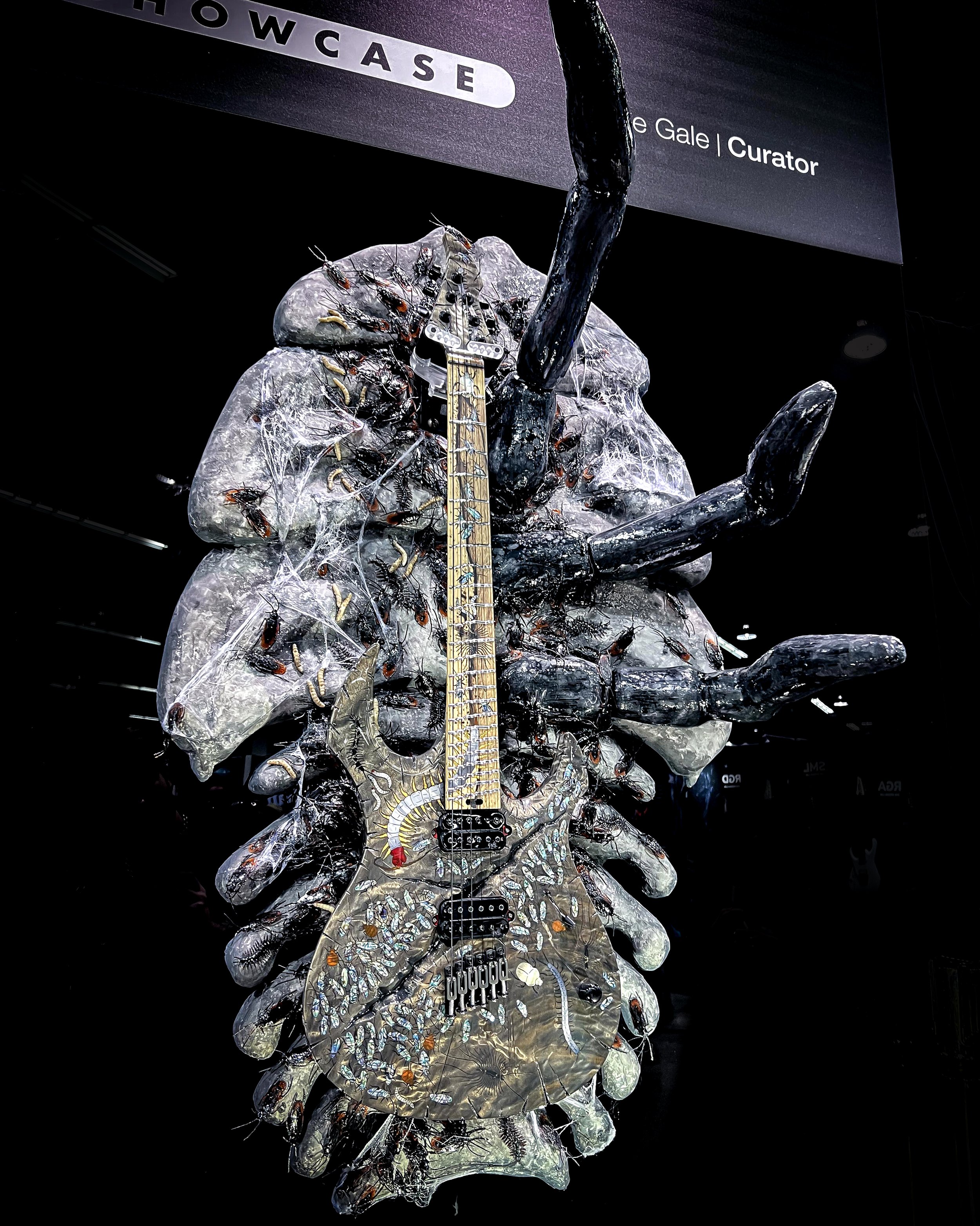 An artistic GNG Giulio Negrini display featuring a guitar embedded with various materials, surrounded by creepy crawly insects, displayed on a pile of ice and rocks.