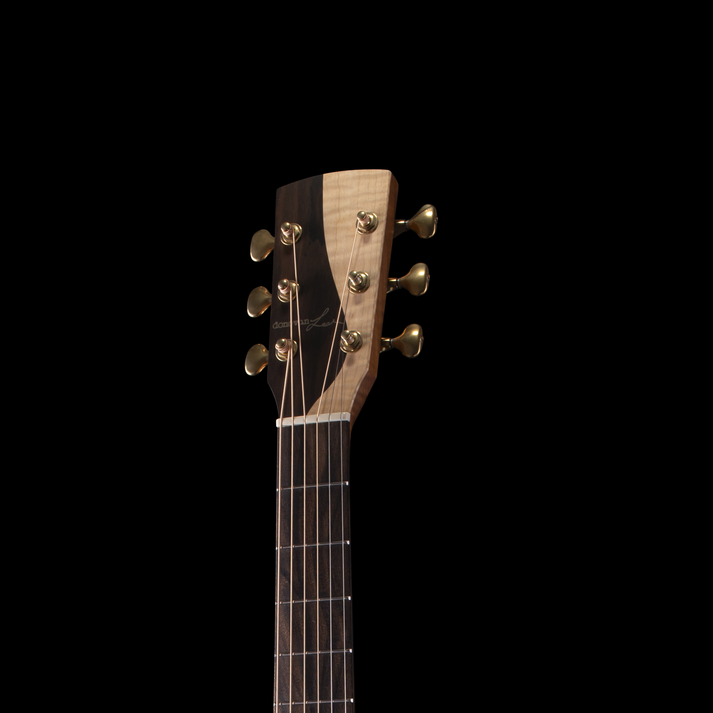 Close-up of a Donovan Leah acoustic Caroline guitar headstock with tuning pegs and strings against a black background.