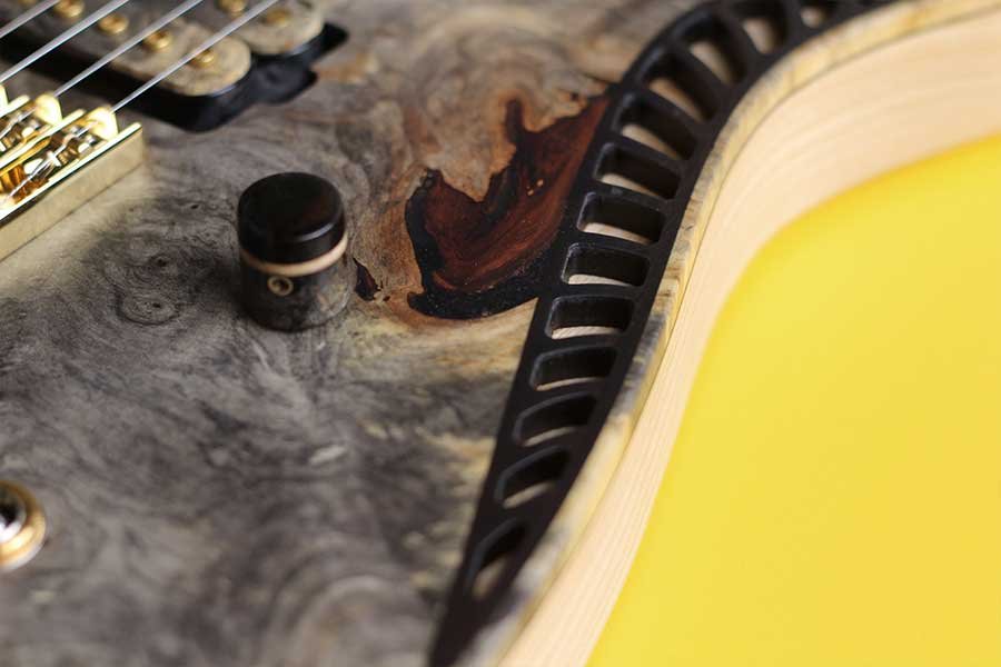 OD Guitars close-up of a guitar body showing wood grain, a black knob, and string bridge with a yellow background.