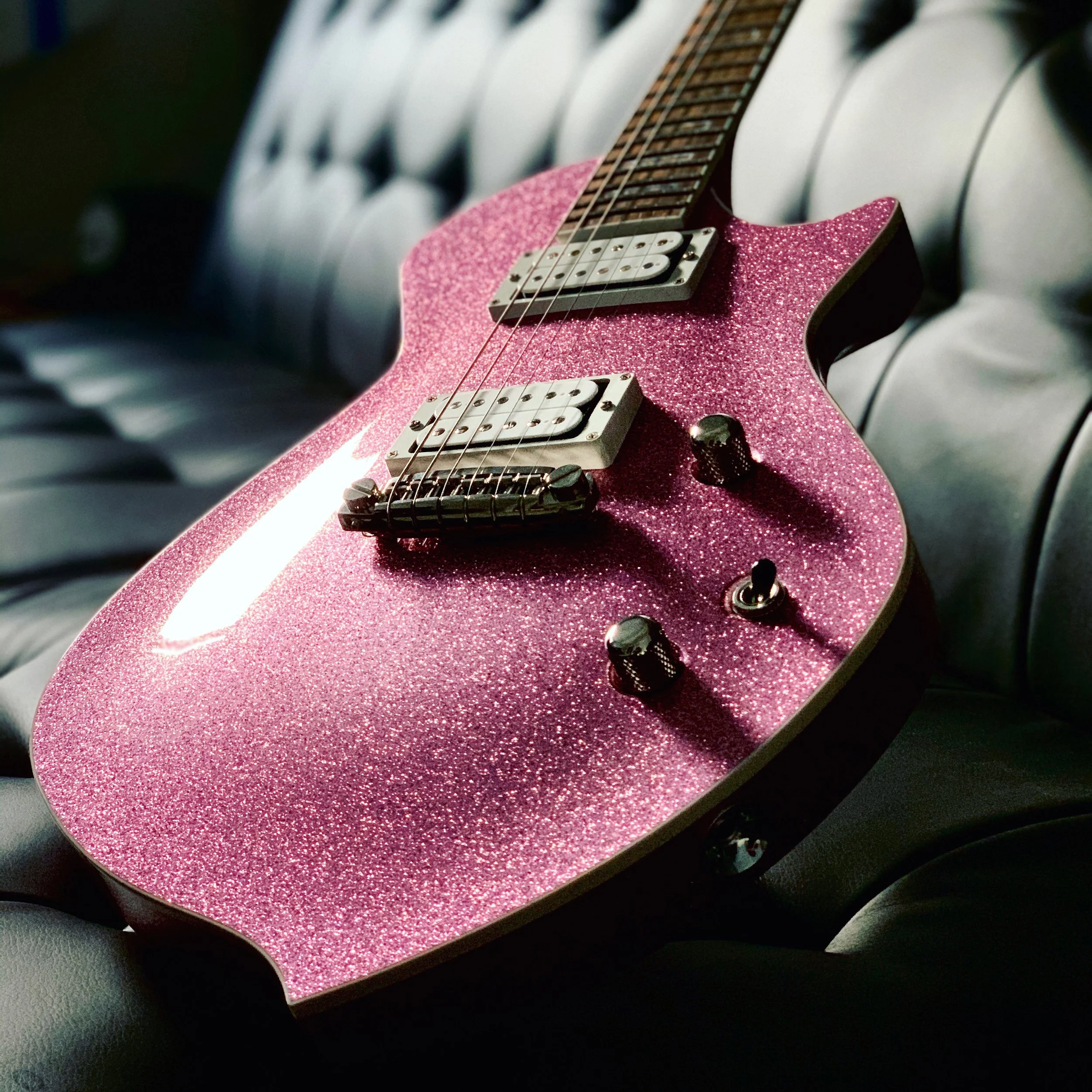 A pink, glittery electric Sully guitar resting on a black leather surface.