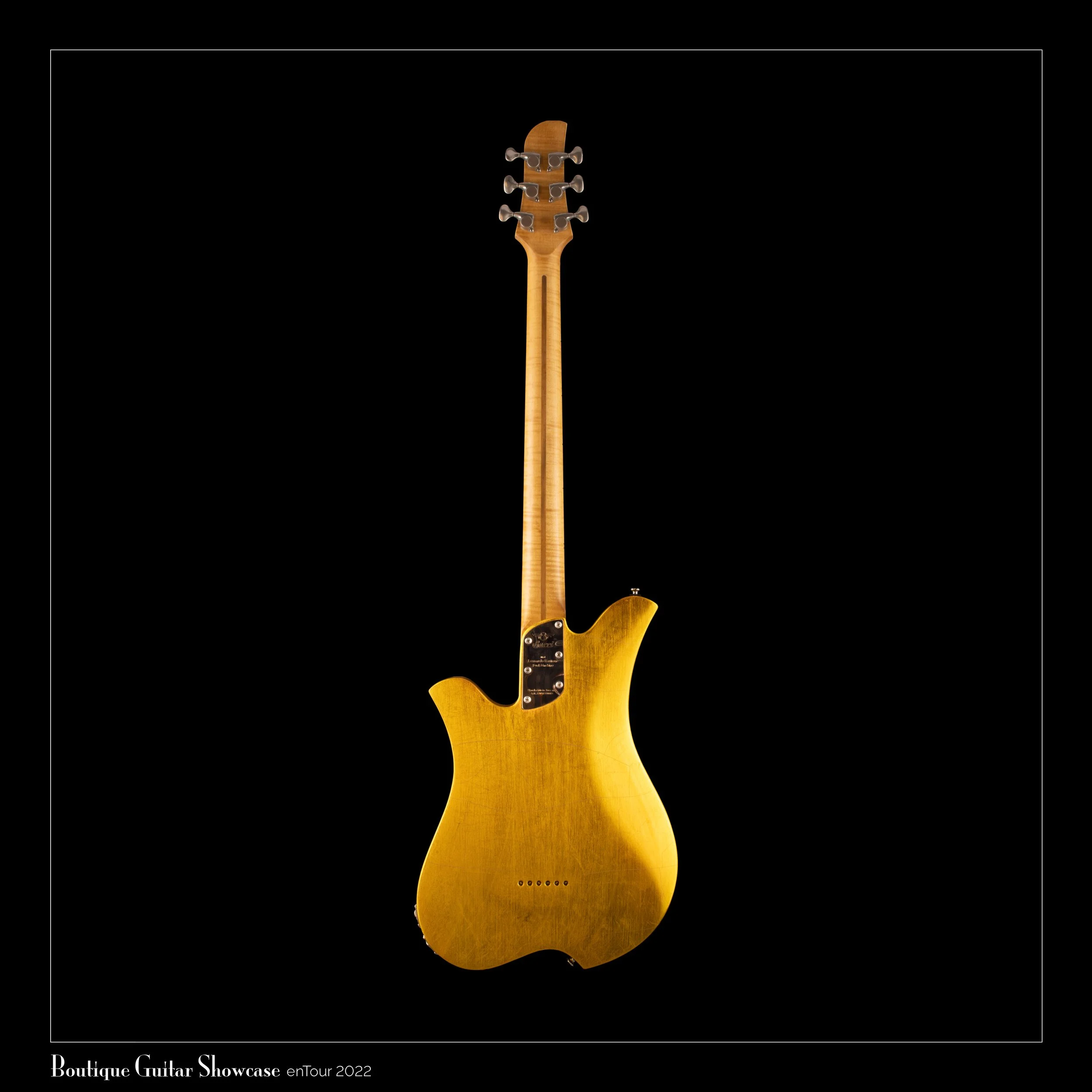 The rear view of a golden Bacci Baritone electric guitar with a wooden finish is displayed against a black background.
