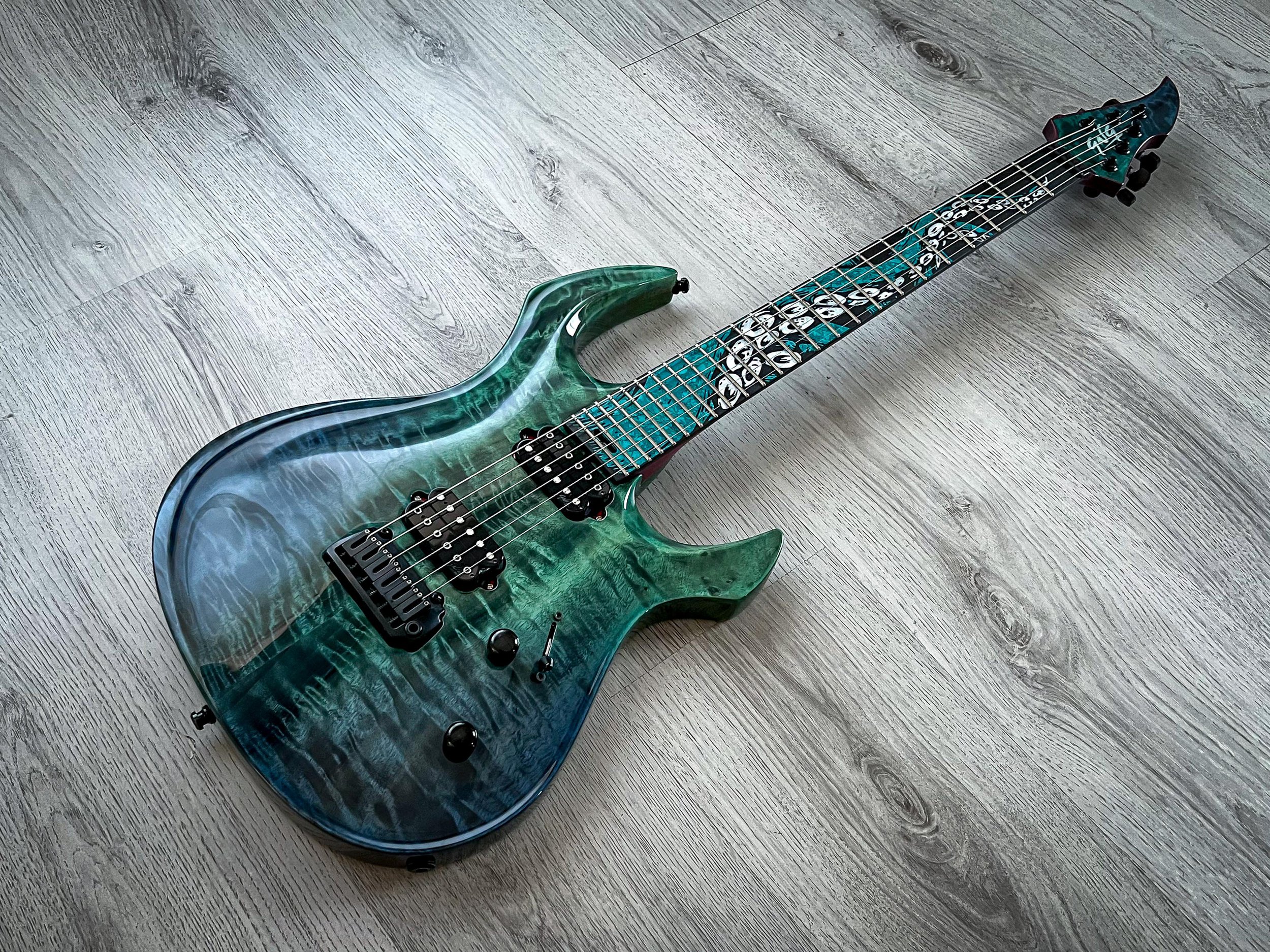 GNG Giulio Negrini electric guitar with a green and blue marbled finish, black hardware, and an intricate design on the fretboard, lying on a light wooden floor.