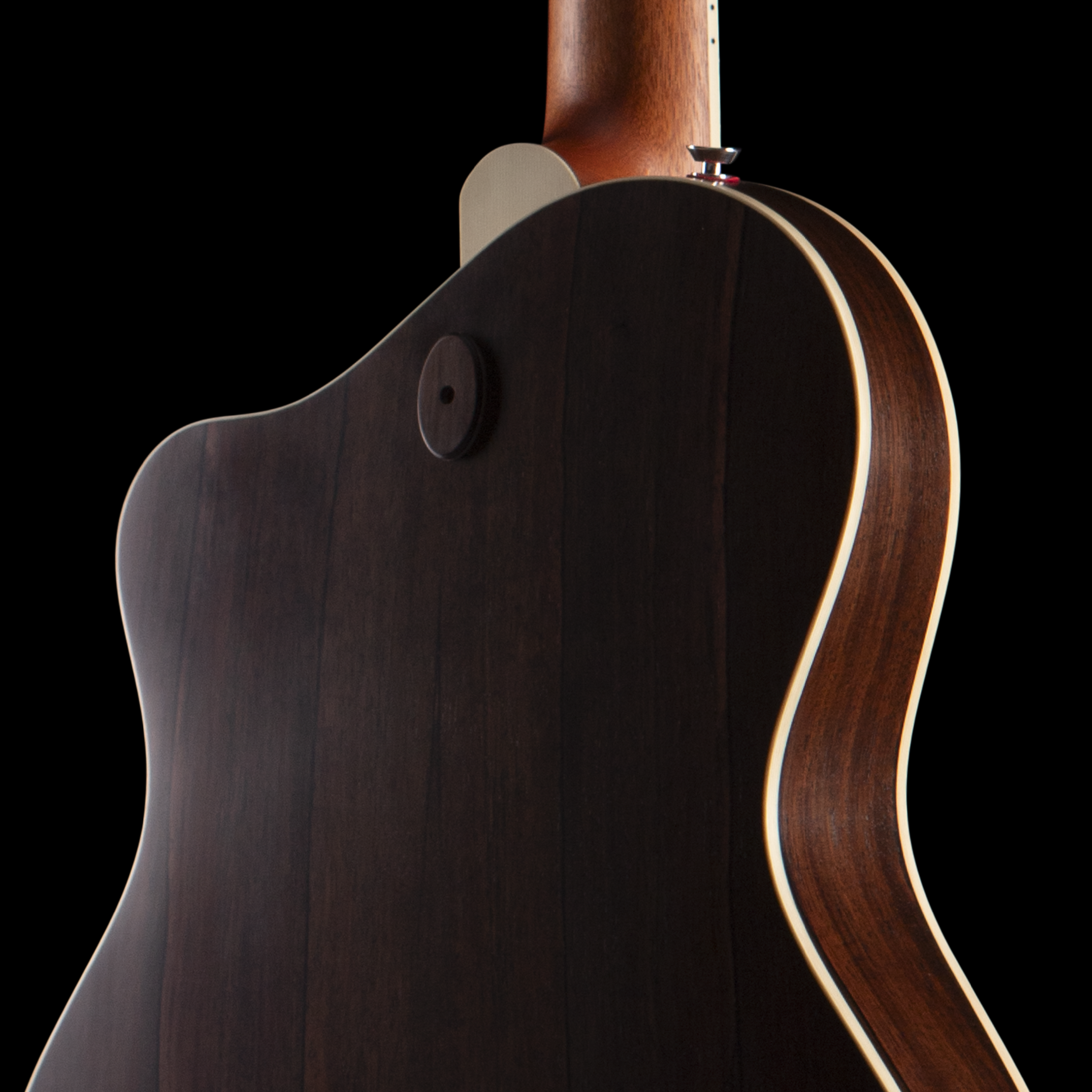 Close-up of an Island Instrument acoustic guitar's body and neck, with focus on the wood grain and curved shape against a black background.