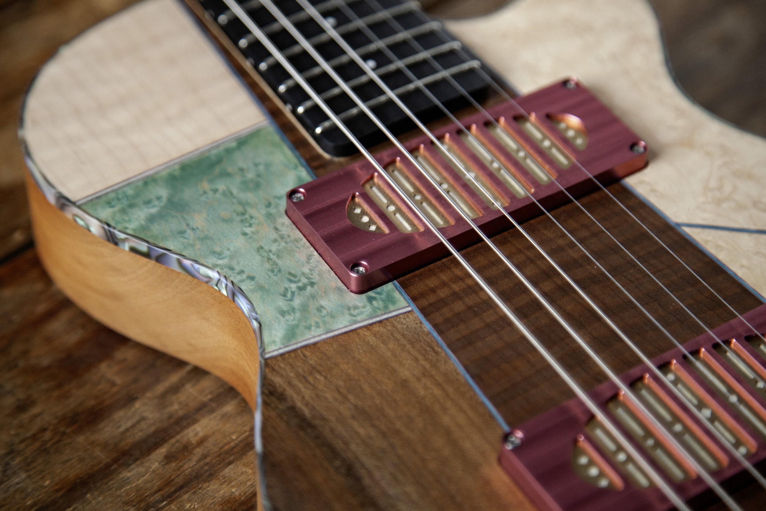 Close-up of an Island Instruments guitar with a colorful pickup installed near the bridge, resting on a wooden surface.