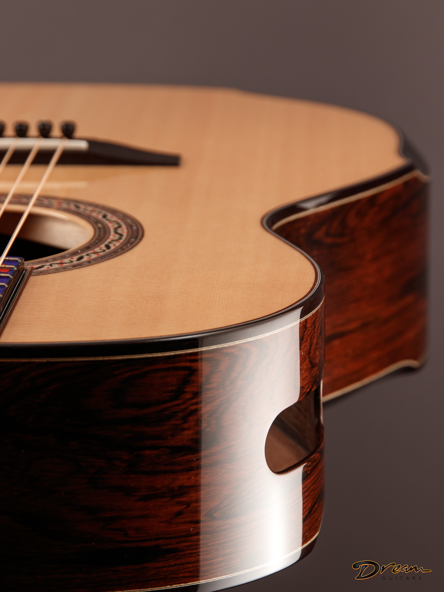 Close-up of an acoustic Laskin guitar body highlighting its wood grain, decorative rosette around the sound hole, and part of the pickguard, with a dark background and a logo in the bottom right corner reading 'Dream Guitars.'